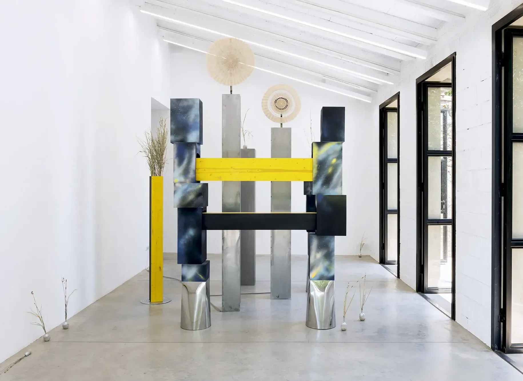 Exhibition review of Leah Dixon: Tartan Tartana at Spiritvessel, Espinavessa, 2026. Steel columns joined by a yellow wood beam beneath a woven wicker wheel.