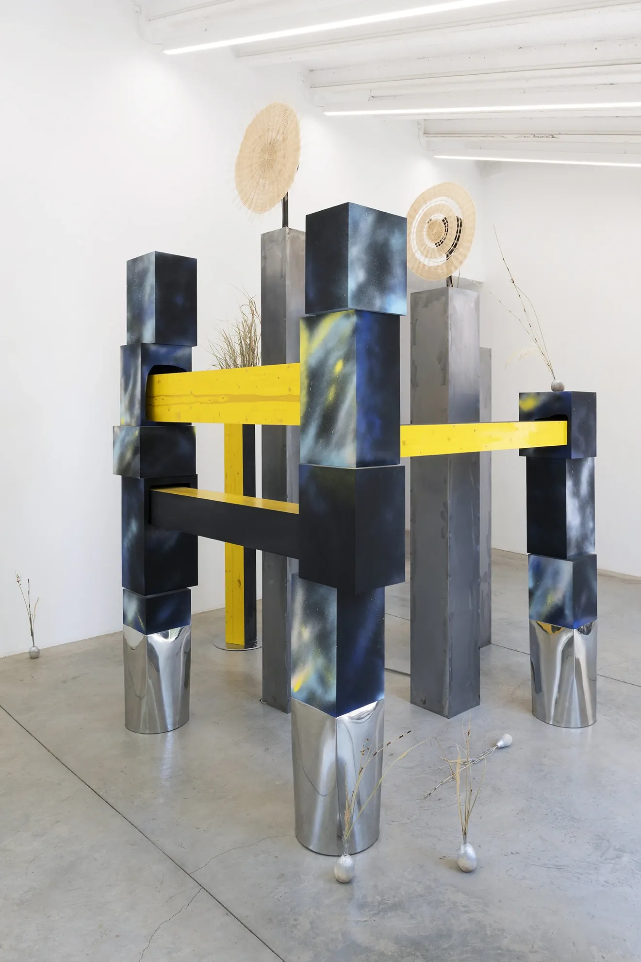 Exhibition review of Leah Dixon: Tartan Tartana at Spiritvessel, Espinavessa, 2026. Marbled steel blocks and mirrored legs support a yellow crossbeam and woven wheel.