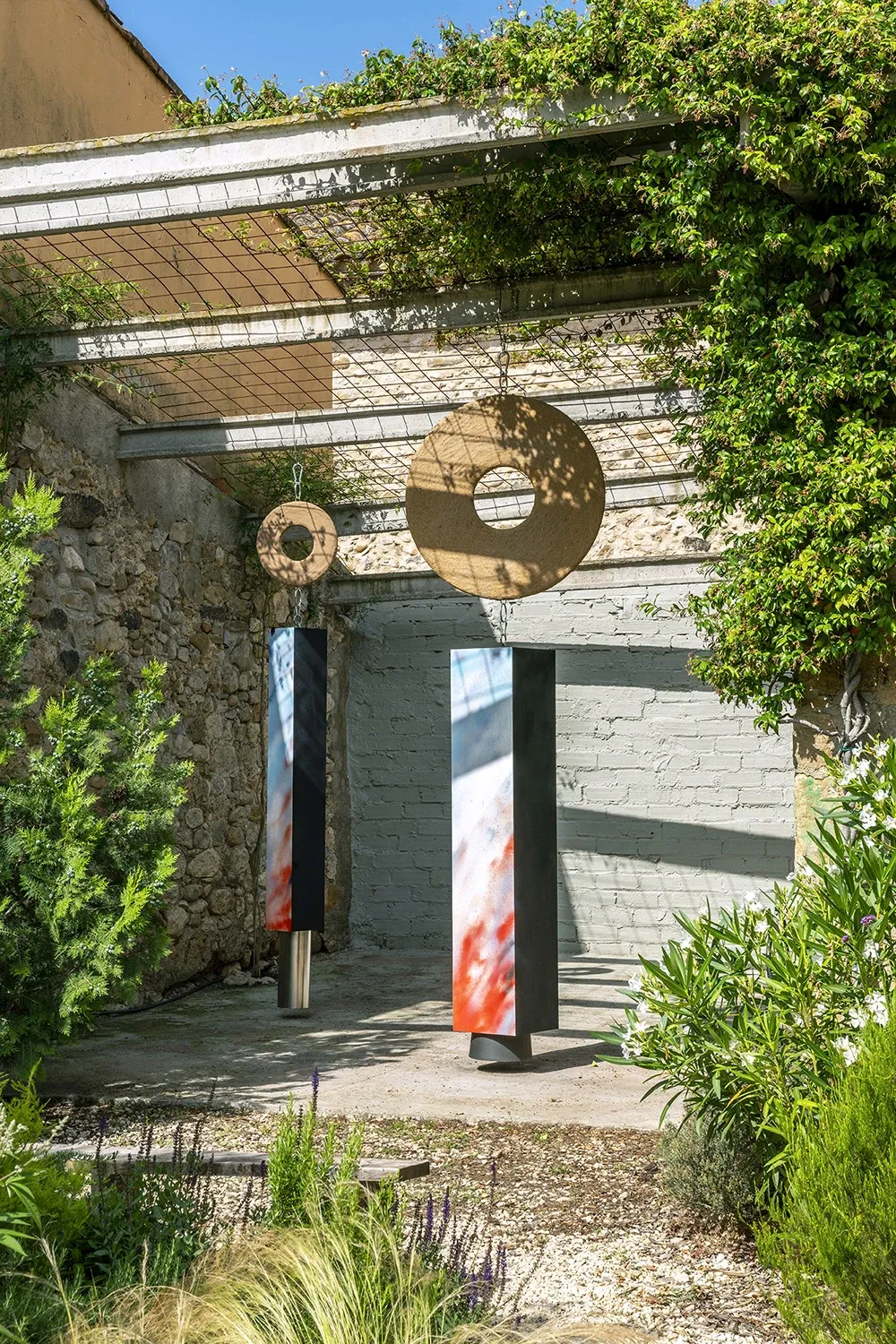 Exhibition review of Leah Dixon: Tartan Tartana at Spiritvessel, Espinavessa, 2026. Suspended discs and vertical panels hang under a pergola against a stone wall.