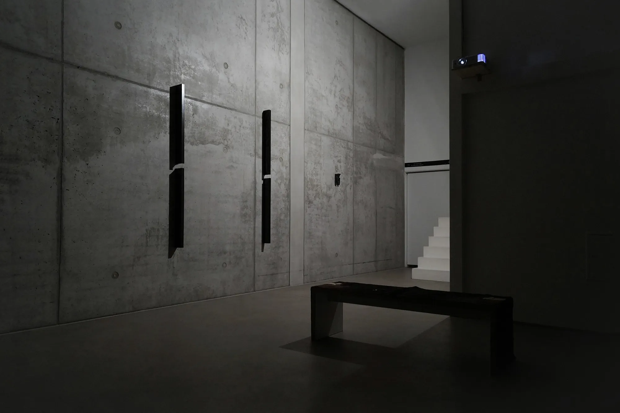 catapult contemporary Exhibition review of Daria Maiier and Sofiia Yesakova: The Solemnity of the Repulsive at ROAM projects e.V., Berlin, 2026. Bare concrete wall with two vertical black wood reliefs and a low bench.