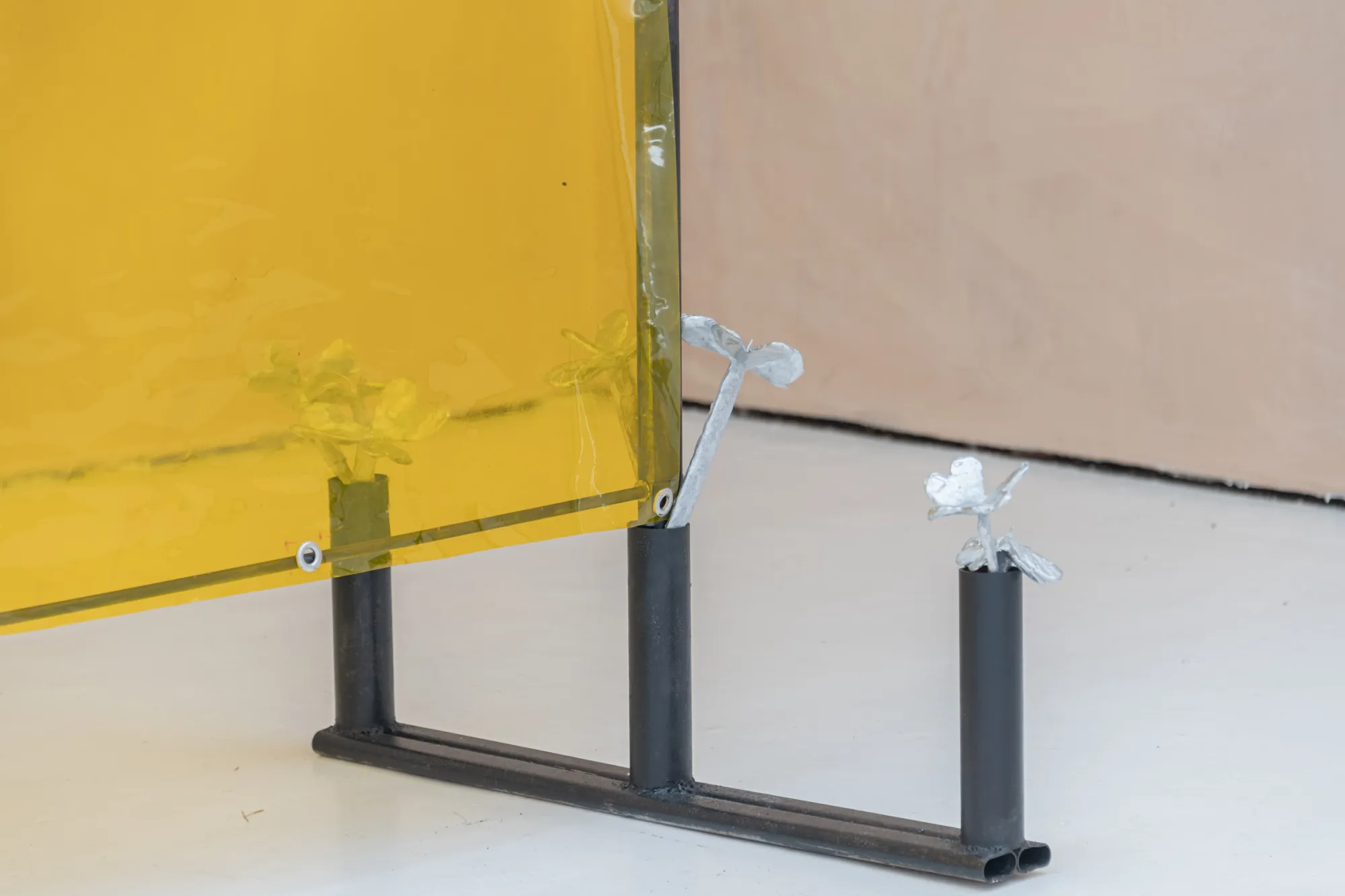 Exhibition review of Maija Fox: As the sap rises at OUTPOST, Norwich, 2026. The steel frame and base of a yellow welding curtain against a white wall