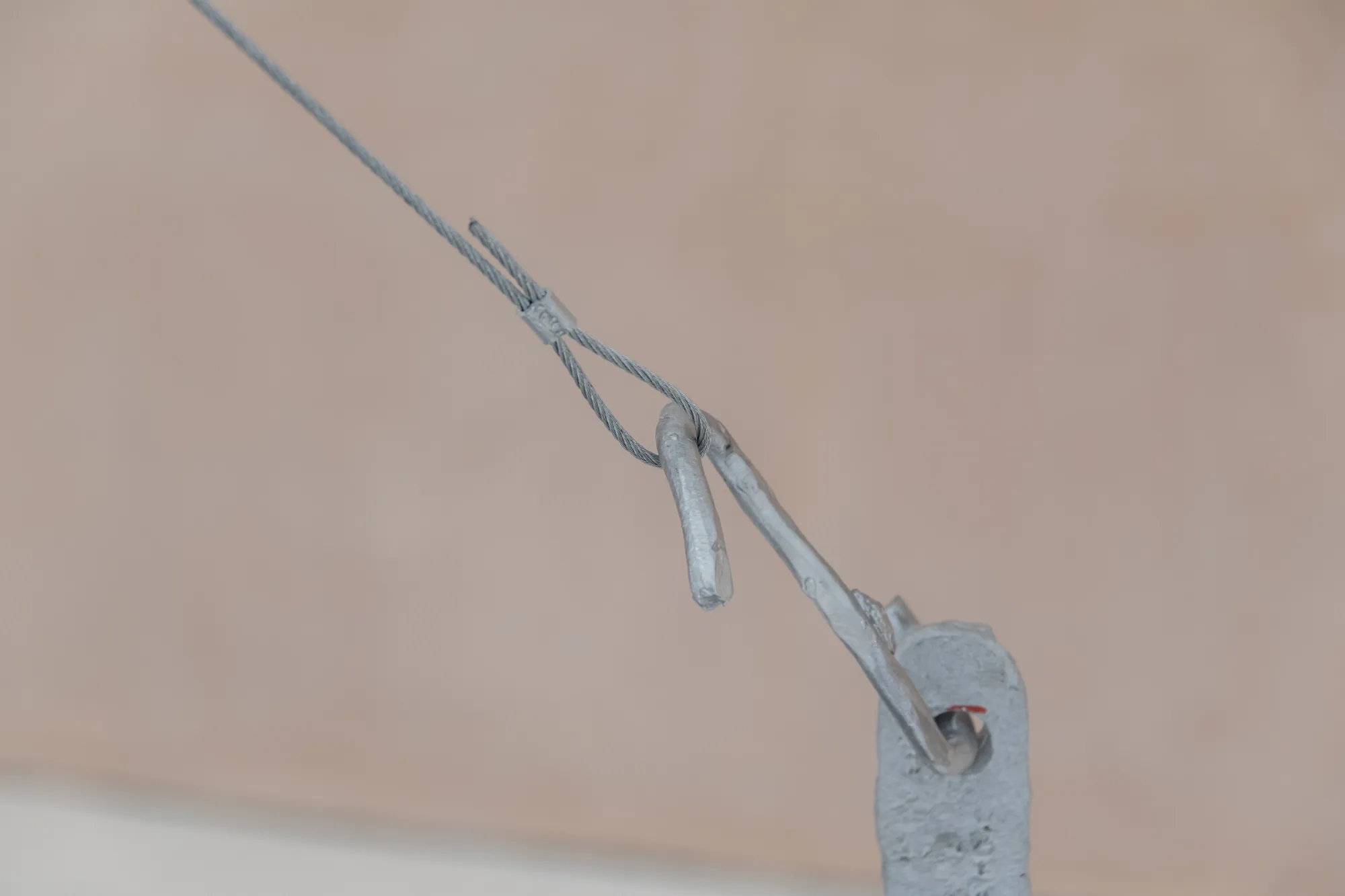 Exhibition review of Maija Fox: As the sap rises at OUTPOST, Norwich, 2026. A steel hook and pulley mechanism suspended on a thin cable.
