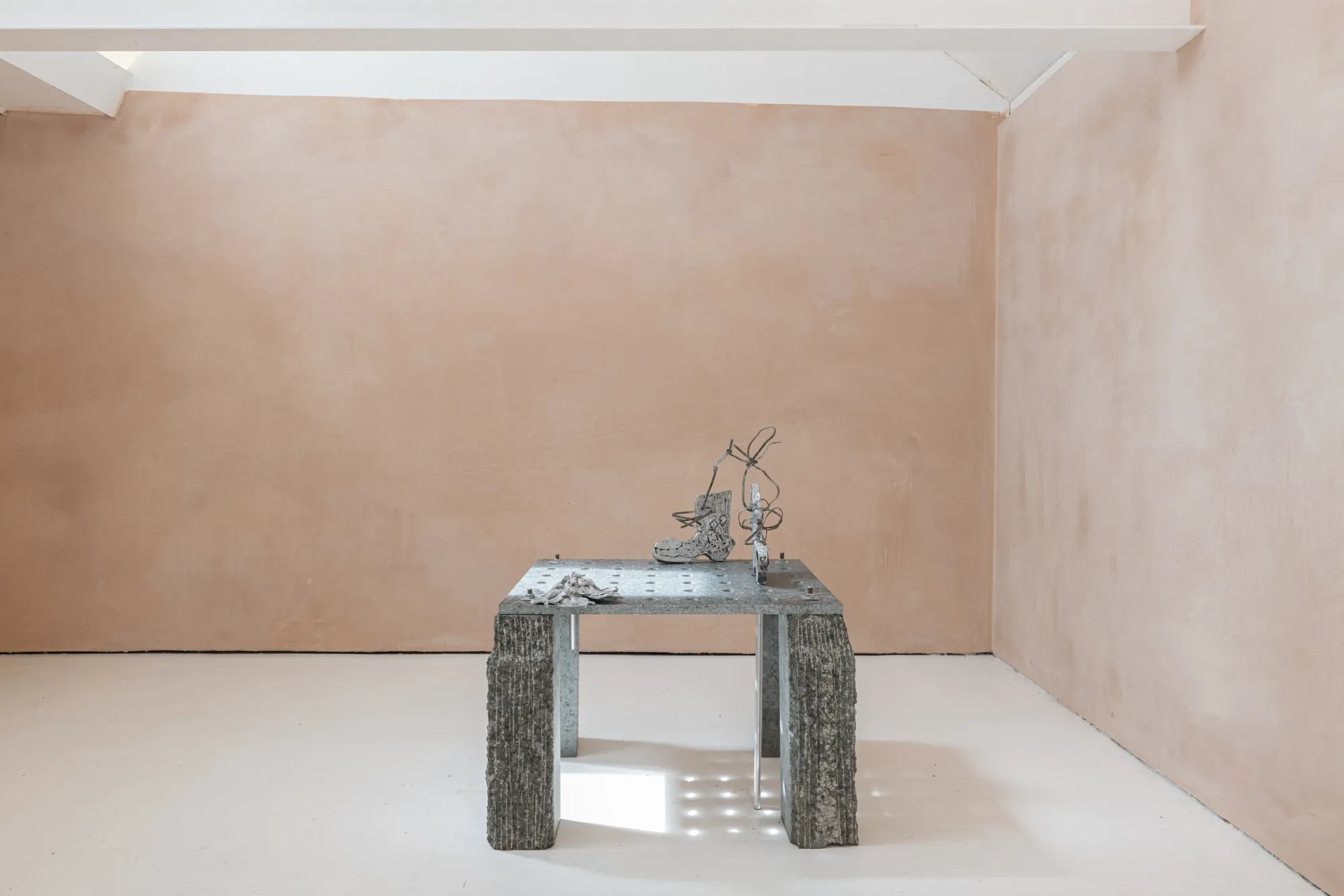 Exhibition review of Maija Fox: As the sap rises at OUTPOST, Norwich, 2026. A granite table with small cast figures seen against a plain pink wall.