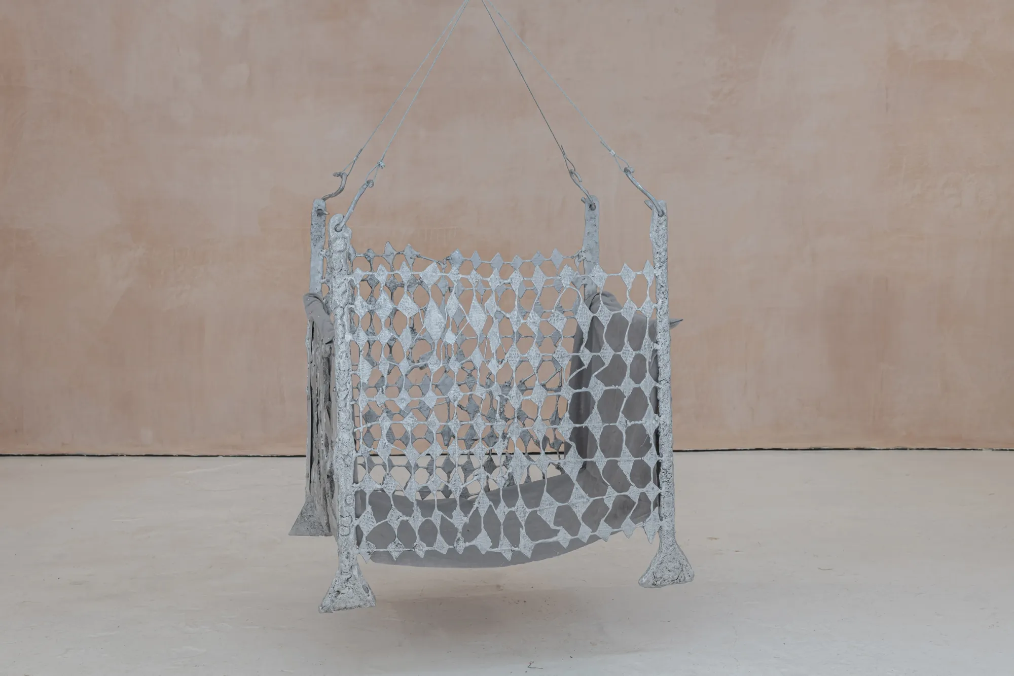 Exhibition review of Maija Fox: As the sap rises at OUTPOST, Norwich, 2026. A folding screen of cast diamond-shaped mesh standing against a plaster wall.