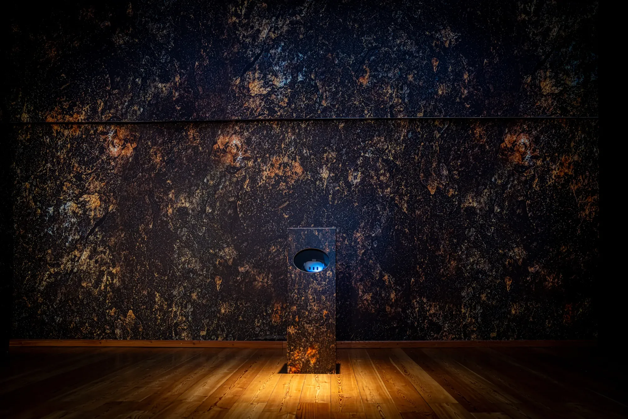 Exhibition review of Marlene Mautner: TRANSFER at Kulturforum Laßnitzhaus, Deutschlandsberg, 2026. Close view of a lit VR pedestal against a dark, mineral-textured wall surface.