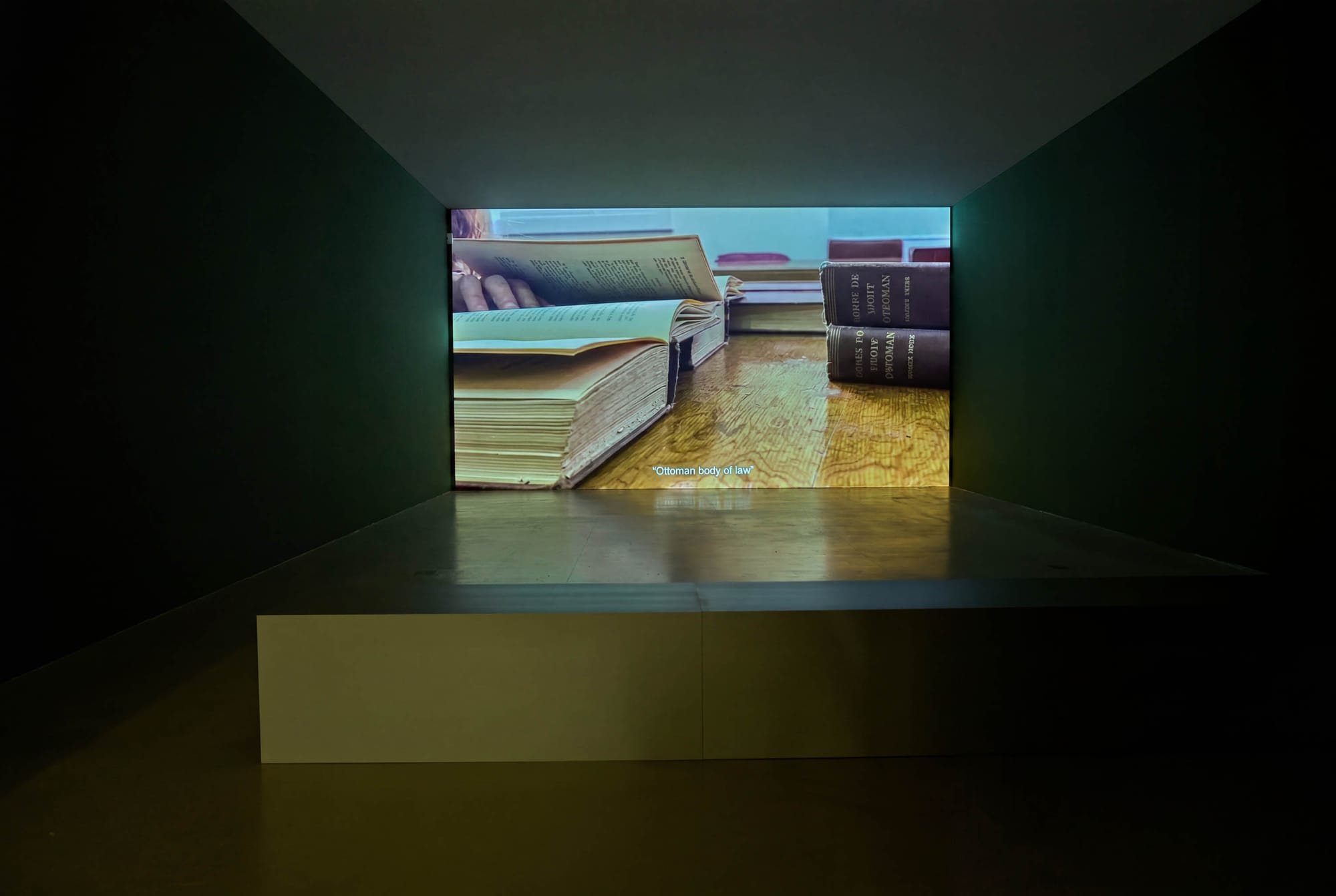 Exhibition review of Marwa Arsanios: Who is Afraid of Ideology? at TAXISPALAIS Kunsthalle Tirol, Innsbruck, 2026. Screen showing open antique law books on a wooden floor, subtitled Ottoman body of law.
