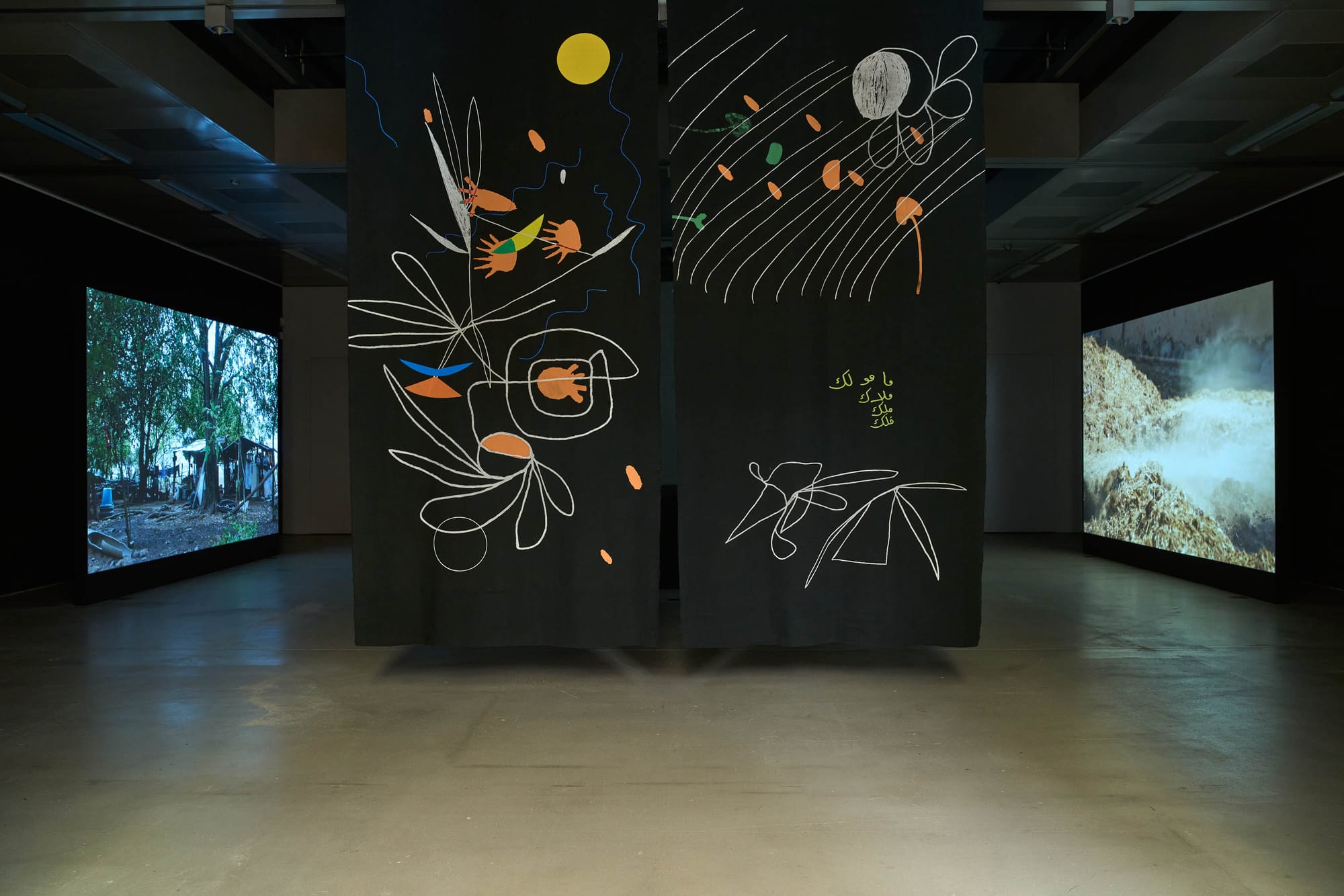 Catapult Exhibition review of Marwa Arsanios: Who is Afraid of Ideology? at TAXISPALAIS Kunsthalle Tirol, Innsbruck, 2026. Green corridor with a hanging ink-printed fabric work and a forest video screen at the far end.