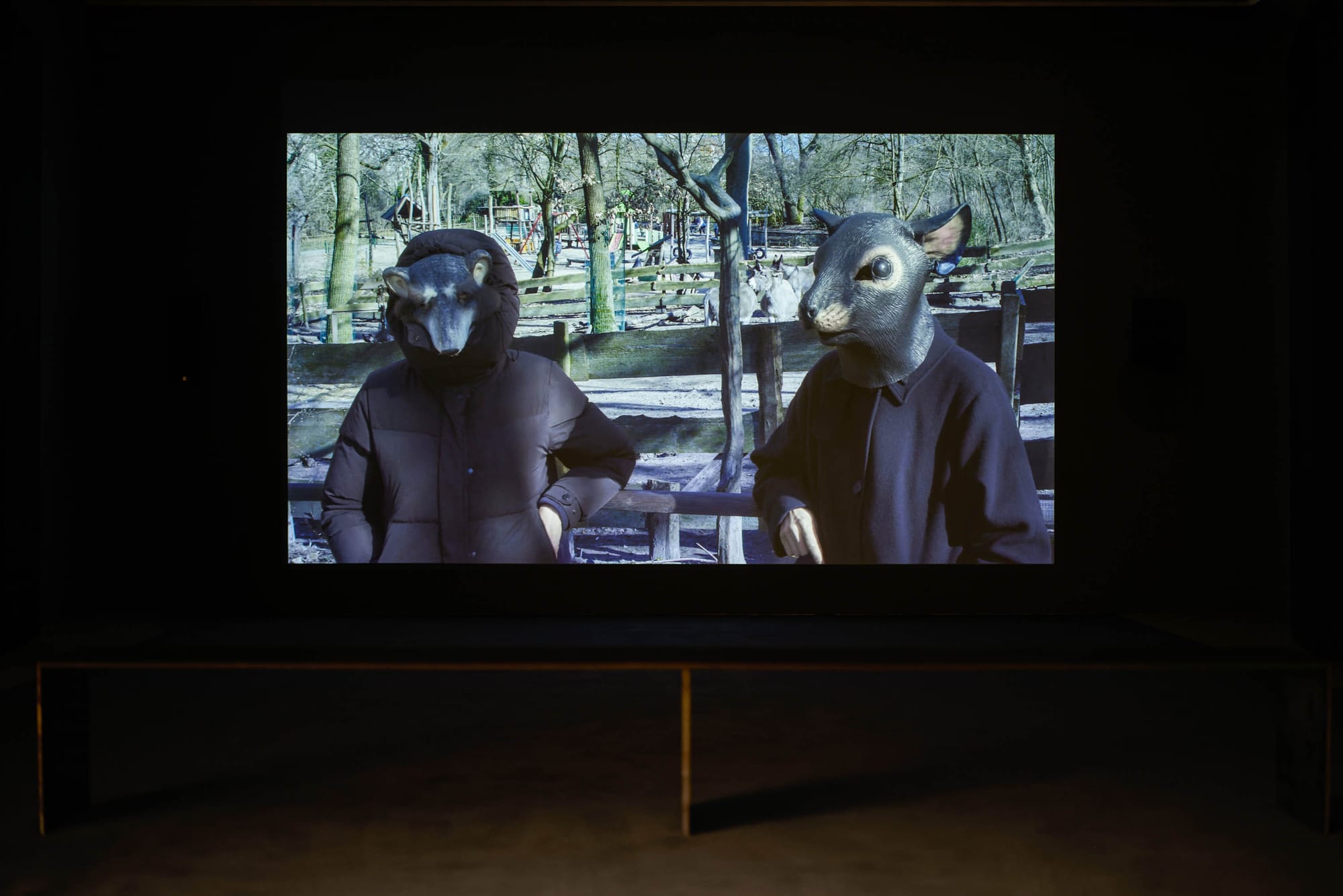 independent catapult Exhibition review of Marwa Arsanios: Who is Afraid of Ideology? at TAXISPALAIS Kunsthalle Tirol, Innsbruck, 2026. Two figures in grey rodent masks and dark coats standing at a wooden park fence.