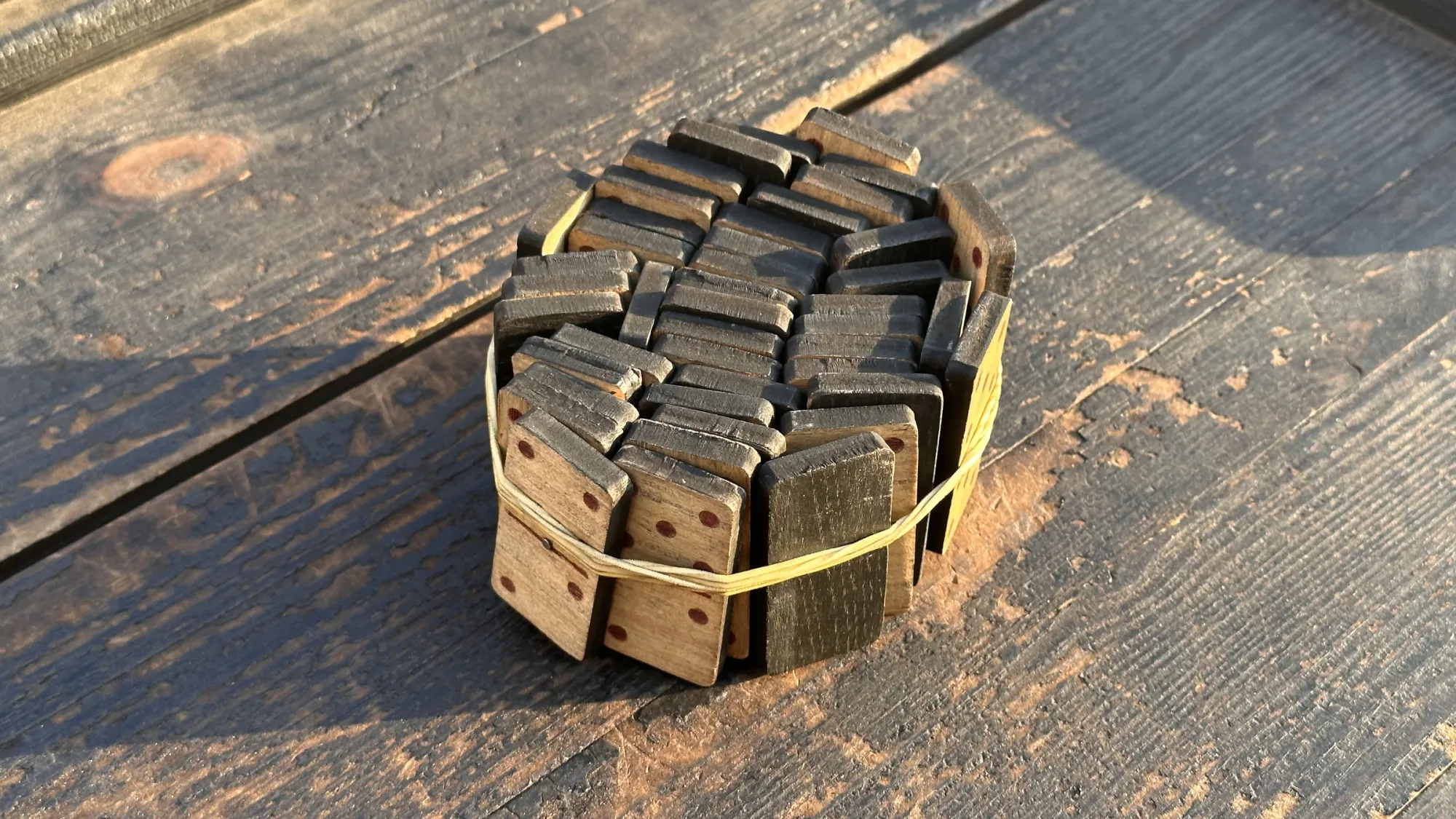 Exhibition review of Nari Ward: Until That Day at DESTE Foundation, Slaughterhouse, Hydra, 2026. Close view of dark wooden domino tiles bound together with a rubber band.