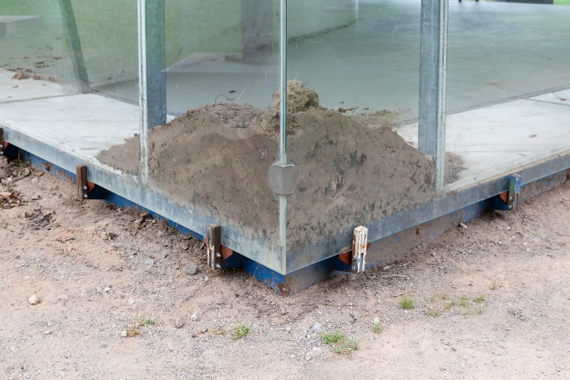 Reparaturgesellschaft, Wewerka Pavilion, Münster, 2026, detail of soil mounded against glass pavilion corner at steel post