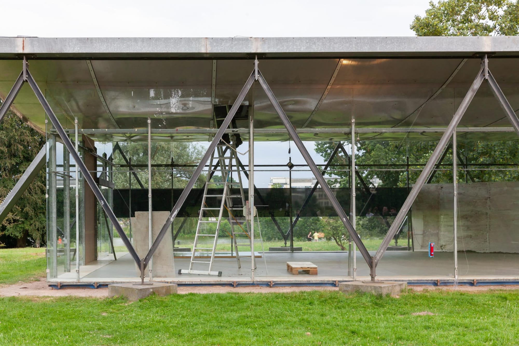 Reparaturgesellschaft, Wewerka Pavilion, Münster, 2026, interior view through steel struts with ladder, wooden pallet, and concrete plinth
