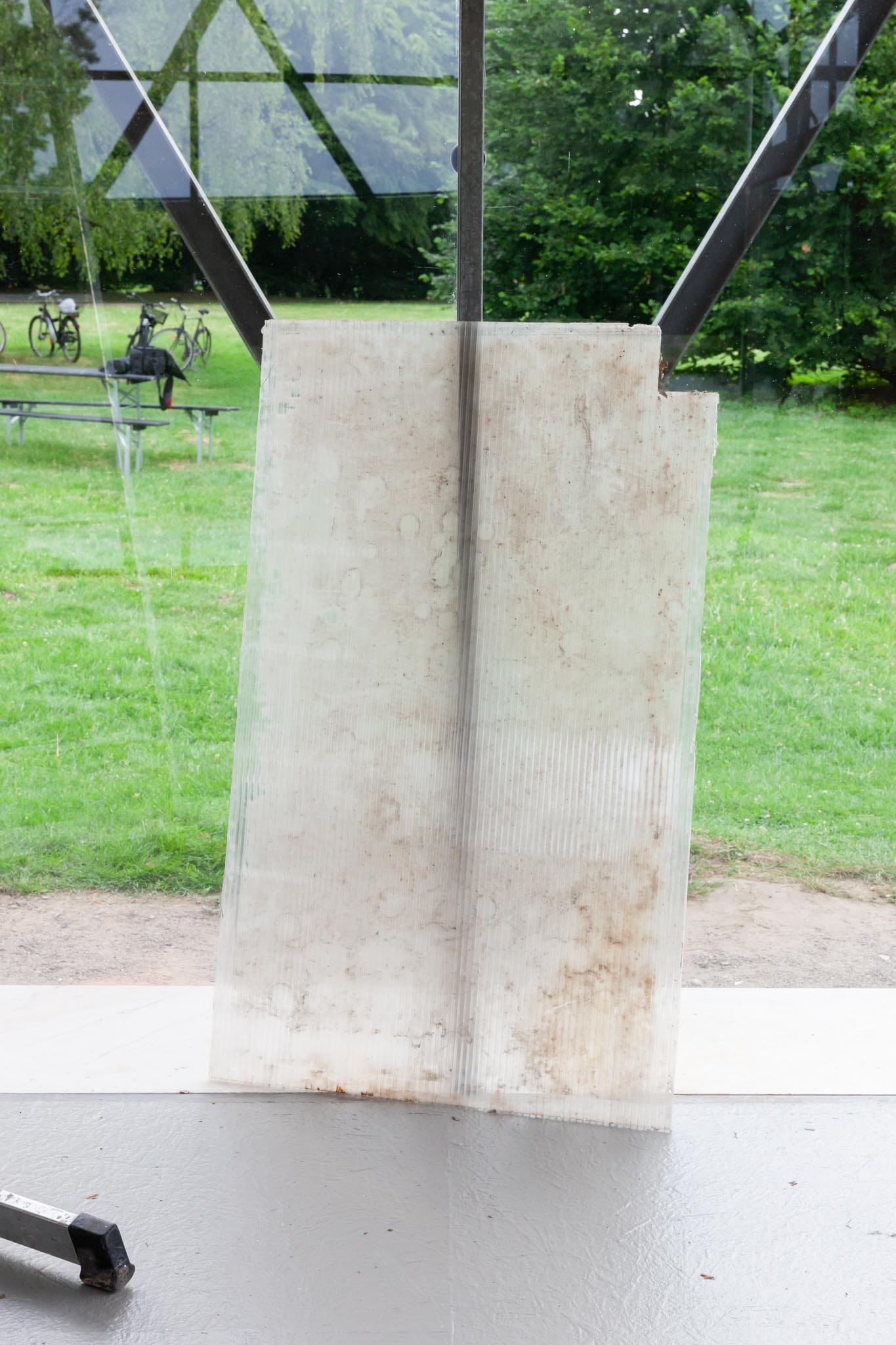 Reparaturgesellschaft, Wewerka Pavilion, Münster, 2026, weathered ribbed glass panel with water stains leaning against steel structural strut