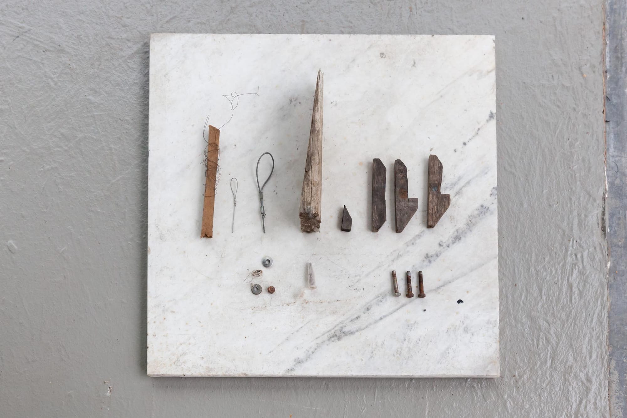 Reparaturgesellschaft, Wewerka Pavilion, Münster, 2026, marble slab with arranged collection of wood fragments, wire loops, screws, and bolts