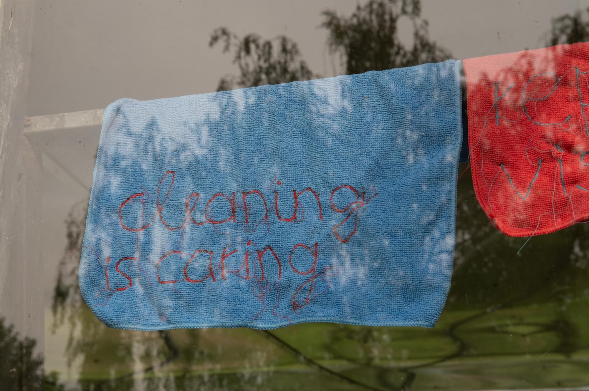 Reparaturgesellschaft, Wewerka Pavilion, Münster, 2026, blue cloth embroidered with the words cleaning is caring, hanging on a line
