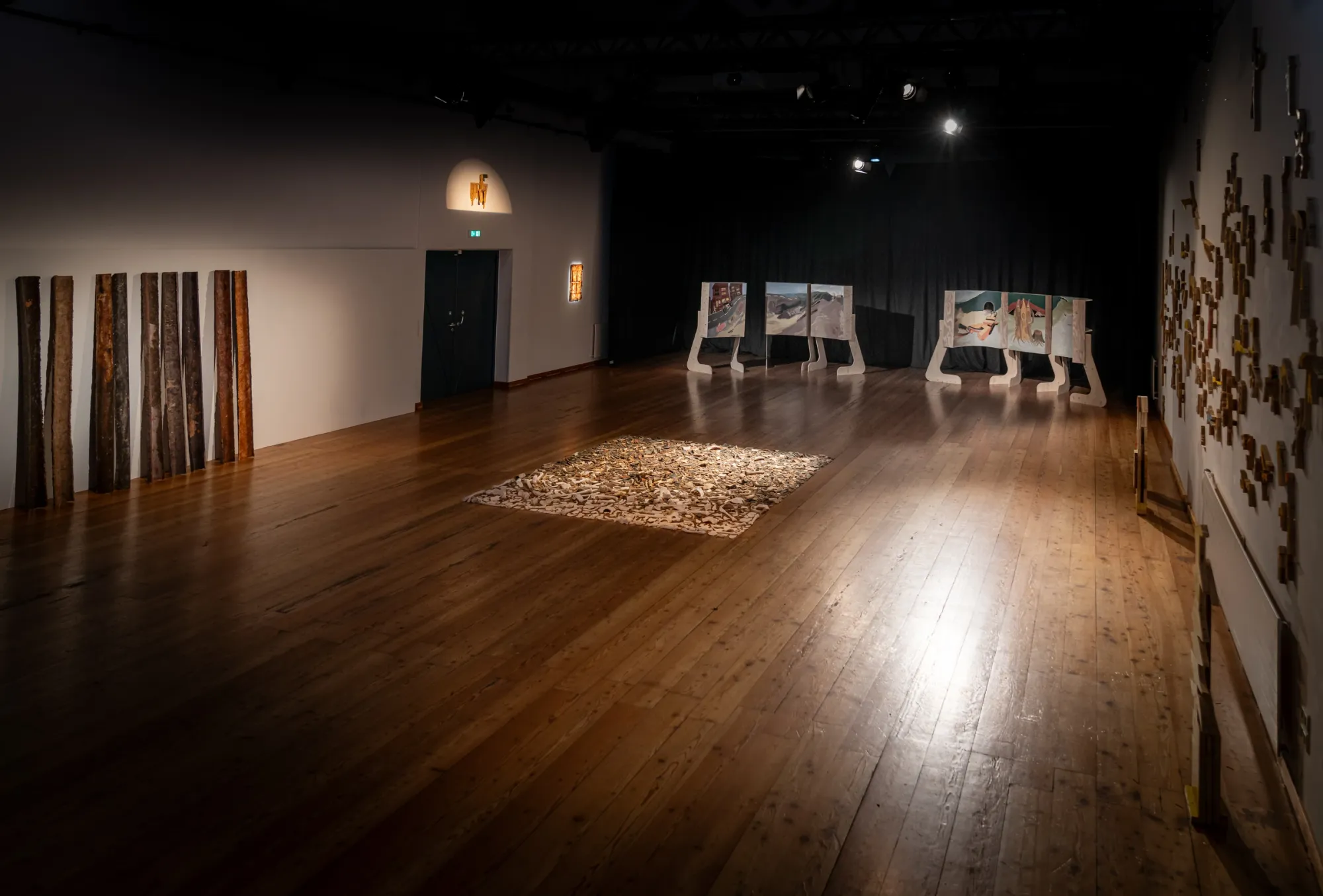 Exhibition review of TRANSFER at Kulturforum Laßnitzhaus, Deutschlandsberg, 2026. Panoramic wall view with dozens of small wood cutout figures spread across the full width of the room.