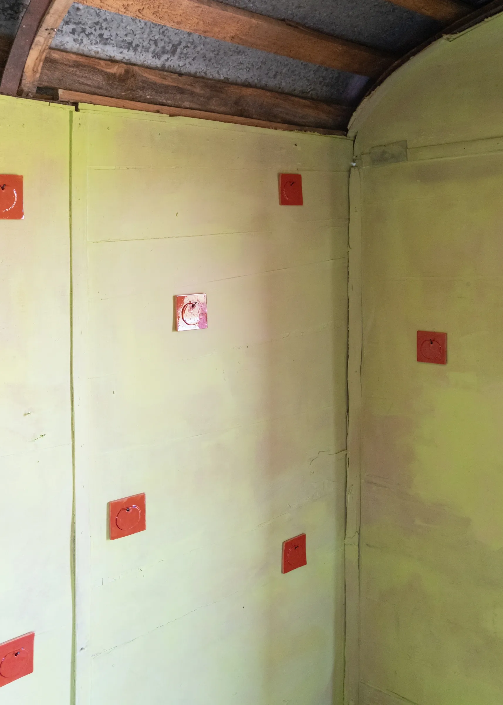 Exhibition review of Tsvetomira Borisova: A Hot Day at lo3eto, Vetren dol, 2026. Several red ceramic apple tiles scattered across a yellow-green wall corner.