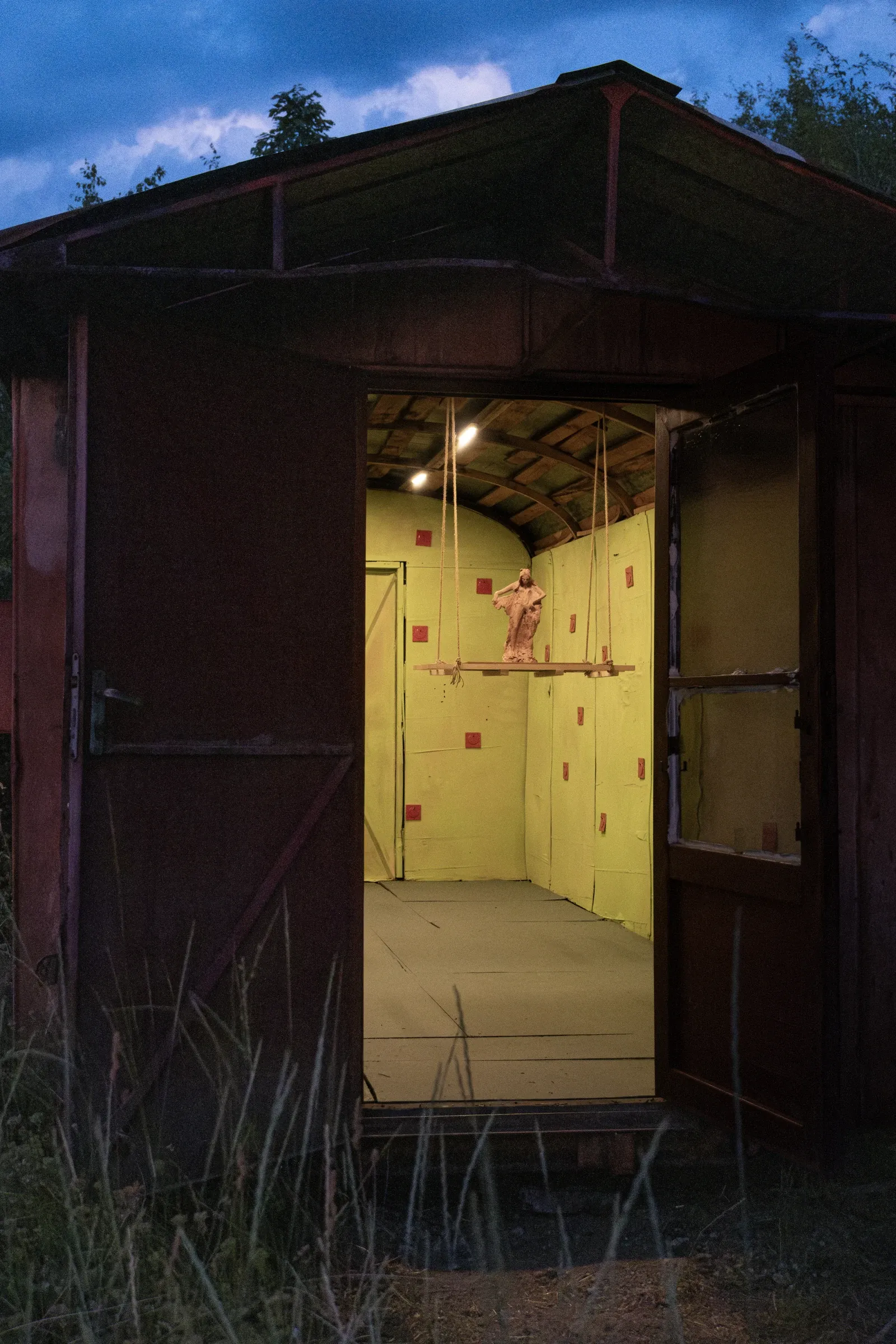 Exhibition review of Tsvetomira Borisova: A Hot Day at lo3eto, Vetren dol, 2026. A dark doorway framing a lit yellow-green room with a suspended red clay figure.