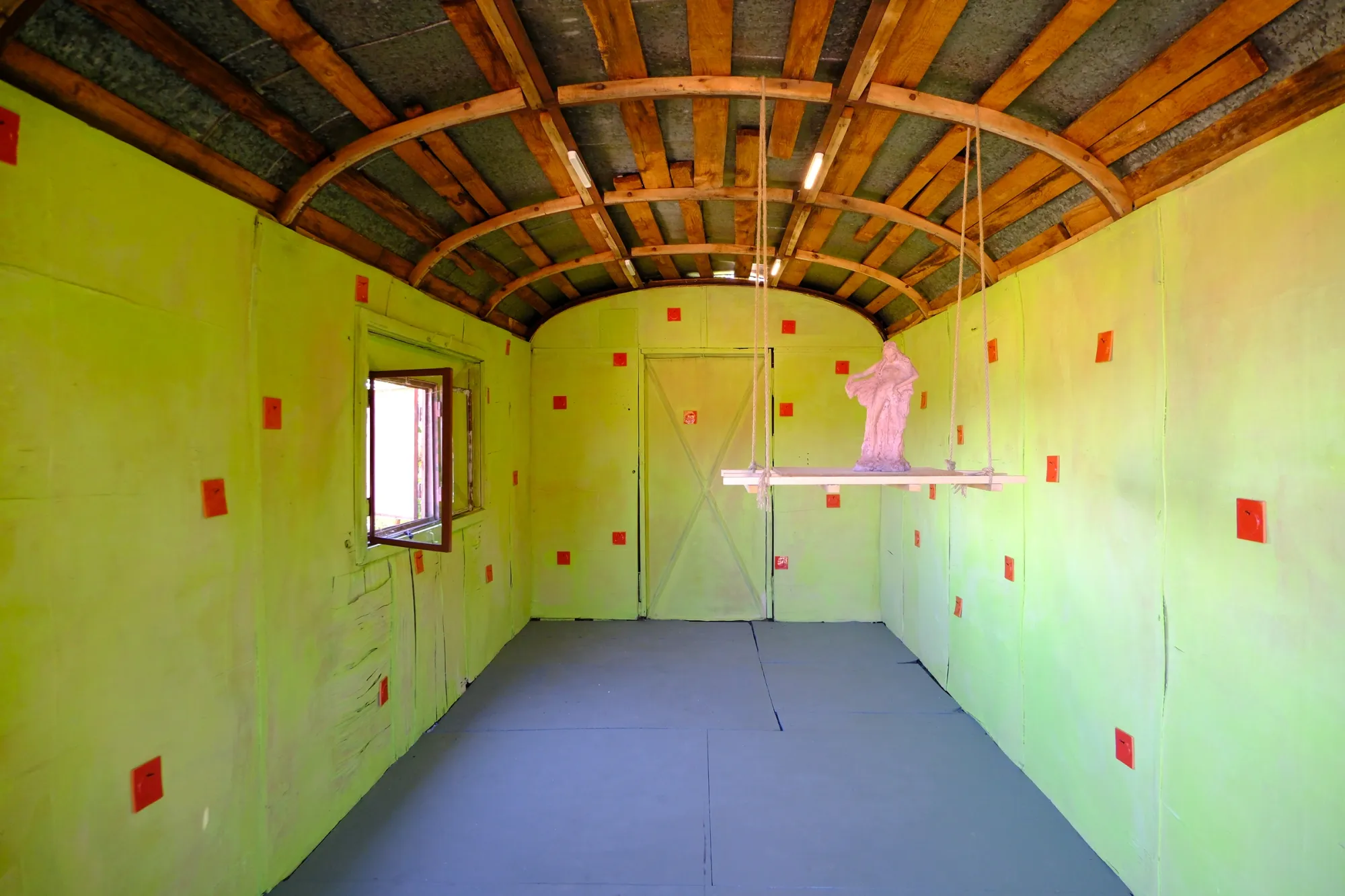 Exhibition review of Tsvetomira Borisova: A Hot Day at lo3eto, Vetren dol, 2026. A yellow-green barrel-vaulted room with a red clay figure on a suspended platform.