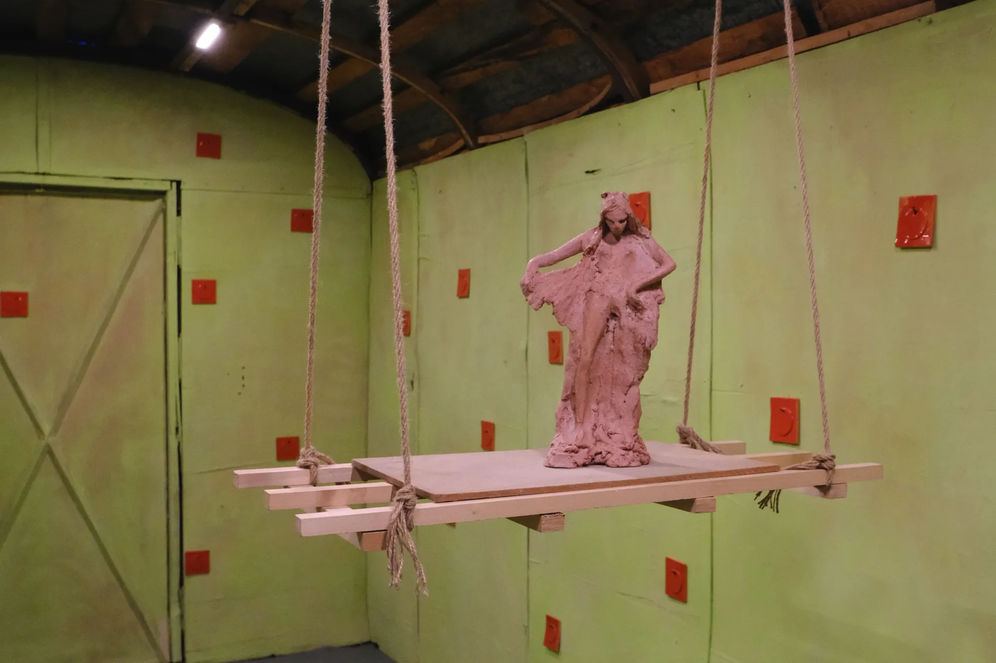 catapult contemporary art platform Exhibition review of Tsvetomira Borisova: A Hot Day at lo3eto, Vetren dol, 2026. Green walls with red ceramic tiles surrounding a suspended clay figure near a door.