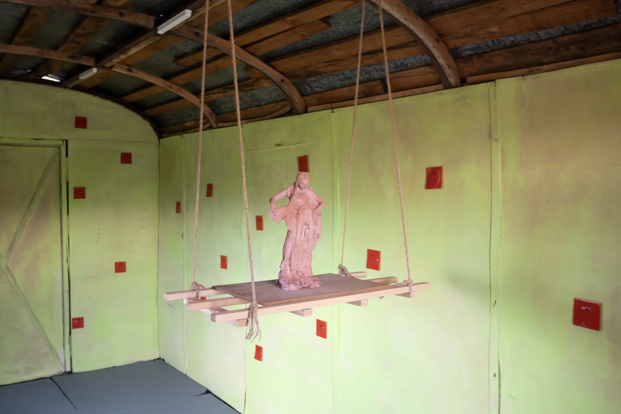 Exhibition review of Tsvetomira Borisova: A Hot Day at lo3eto, Vetren dol, 2026. Wide view of the green room with ceiling beams, floor and the hanging sculpture.