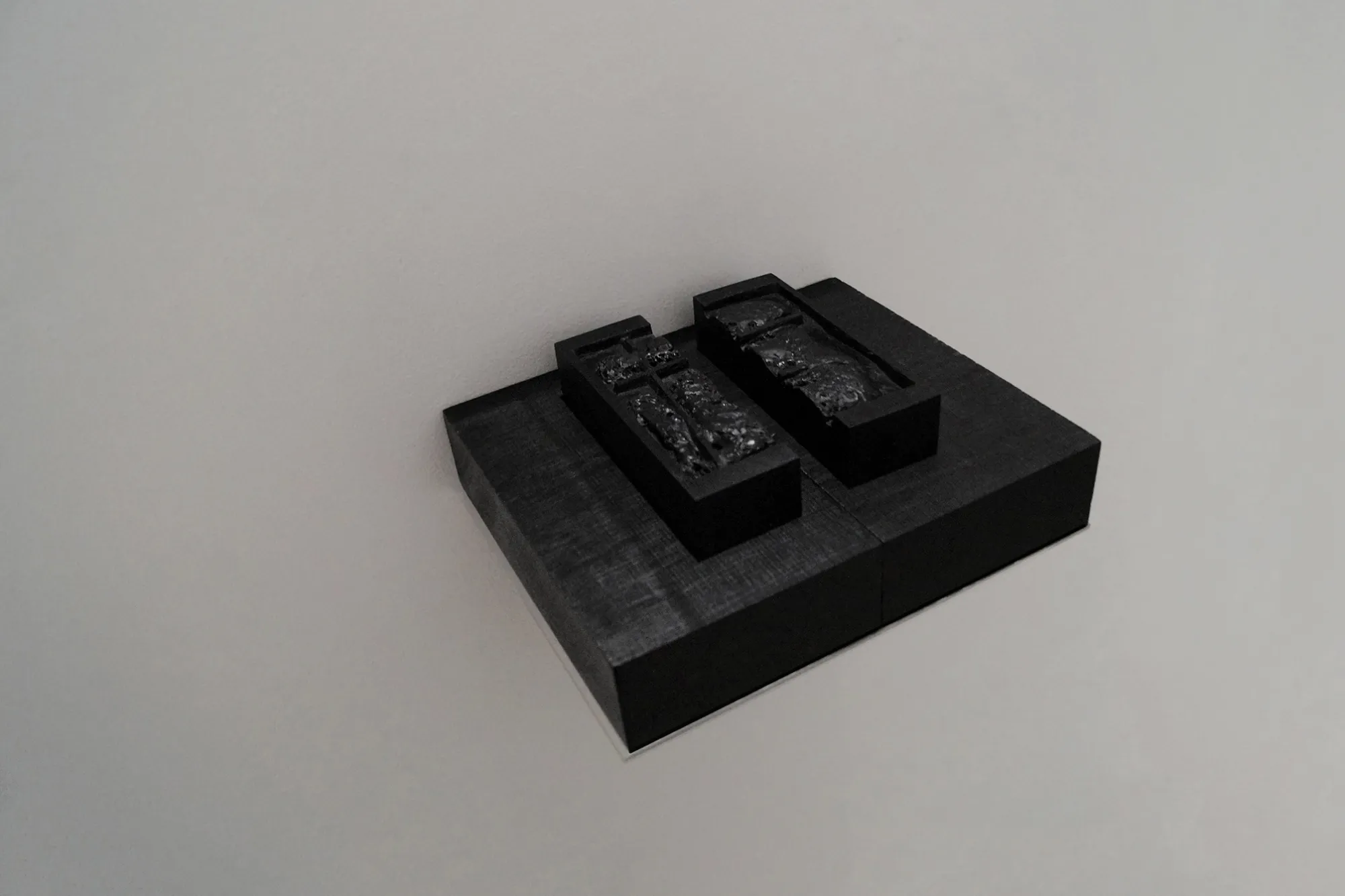 Exhibition review of Sofiia Yesakova: The Solemnity of the Repulsive at ROAM projects e.V., Berlin, 2026. Two dark wooden boxes on a wall shelf, each holding a textured black arch-shaped relief.
