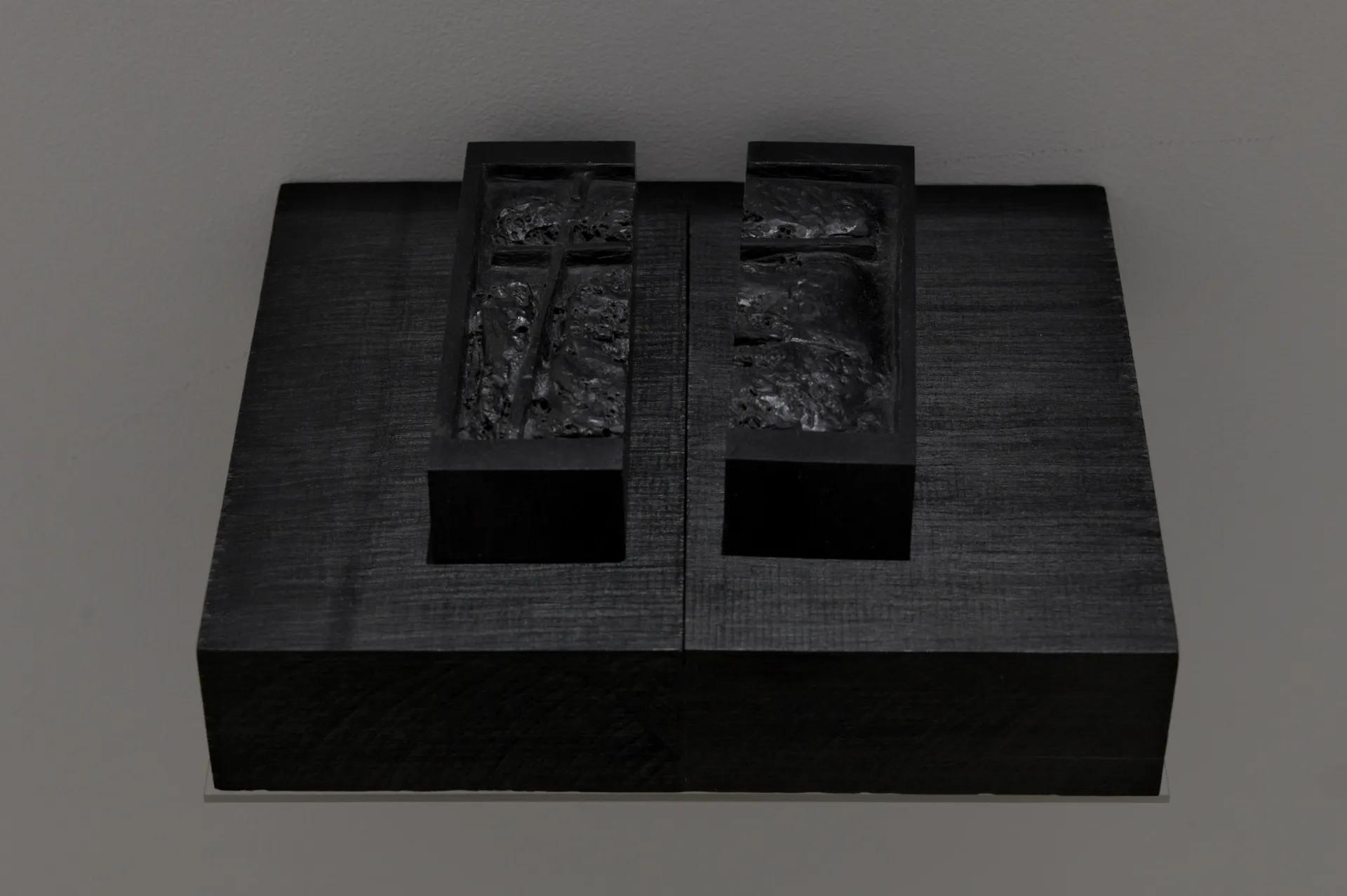 Exhibition review of Sofiia Yesakova: The Solemnity of the Repulsive at ROAM projects e.V., Berlin, 2026. Overhead detail of two wooden boxes with pale arch shapes set into black gelatine relief.