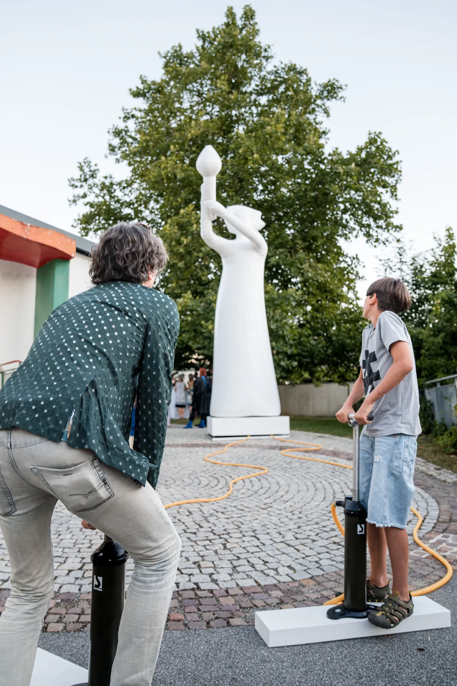Exhibition review of zweintopf: TRANSFER at Kulturforum Laßnitzhaus, Deutschlandsberg, 2026. A tall white inflatable figure with a raised arm standing outdoors against trees.