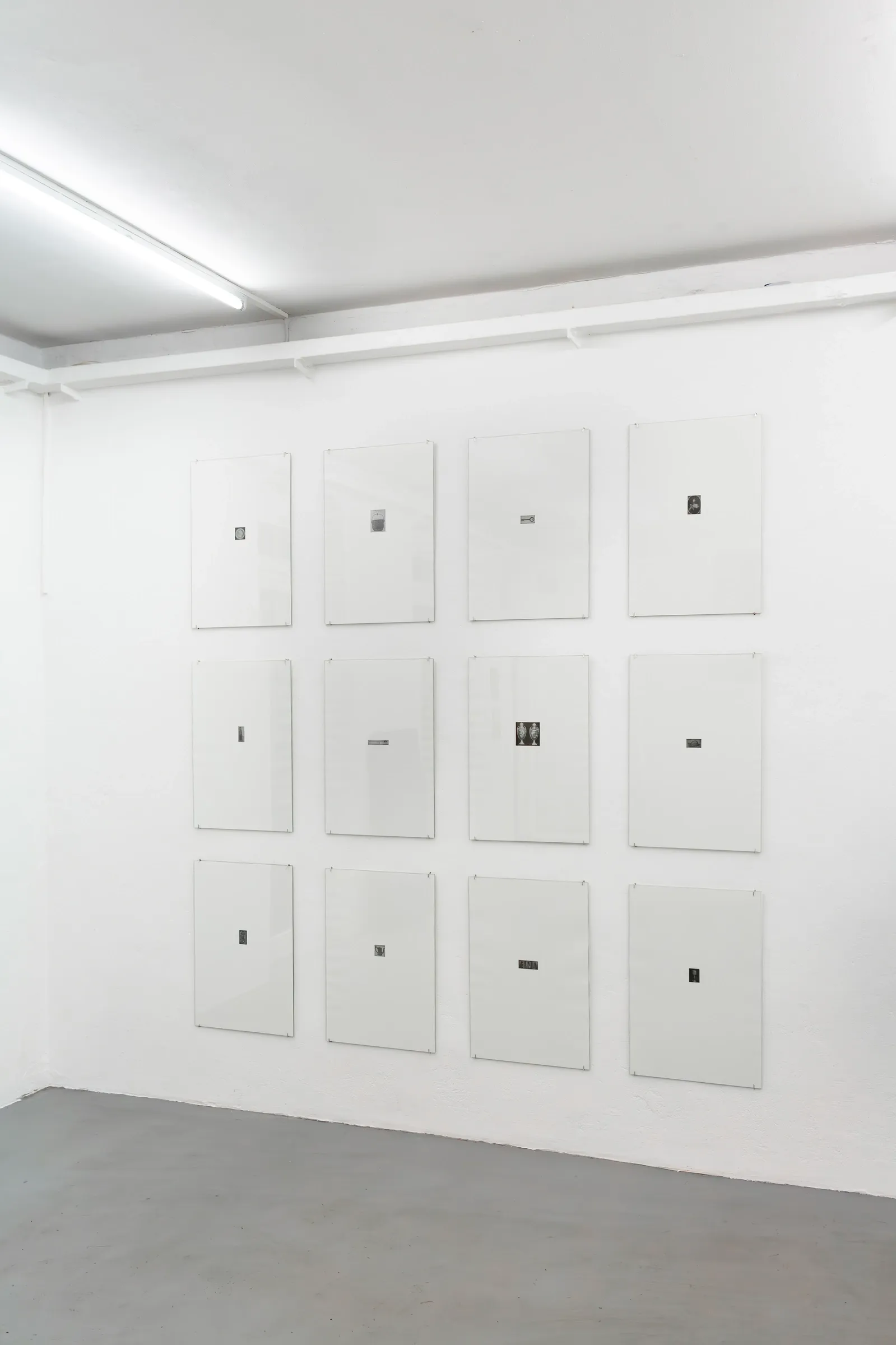 Exhibition review of Anastasia Sosunova: A Charm of Powerful Trouble at ACUD Galerie, Berlin, 2026. A grid of twelve small photozincography prints under glass on a white wall beside a white door.