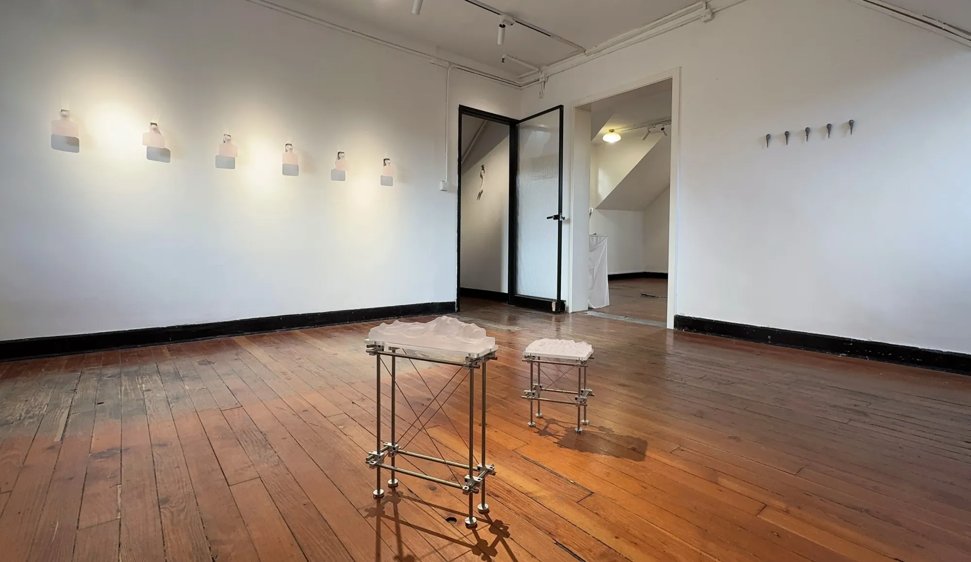 Exhibition review of Eva Chenyao He: Procrustean at COLLECTA, Shanghai, 2026. Six pale glass ear tags in a row on a white wall.