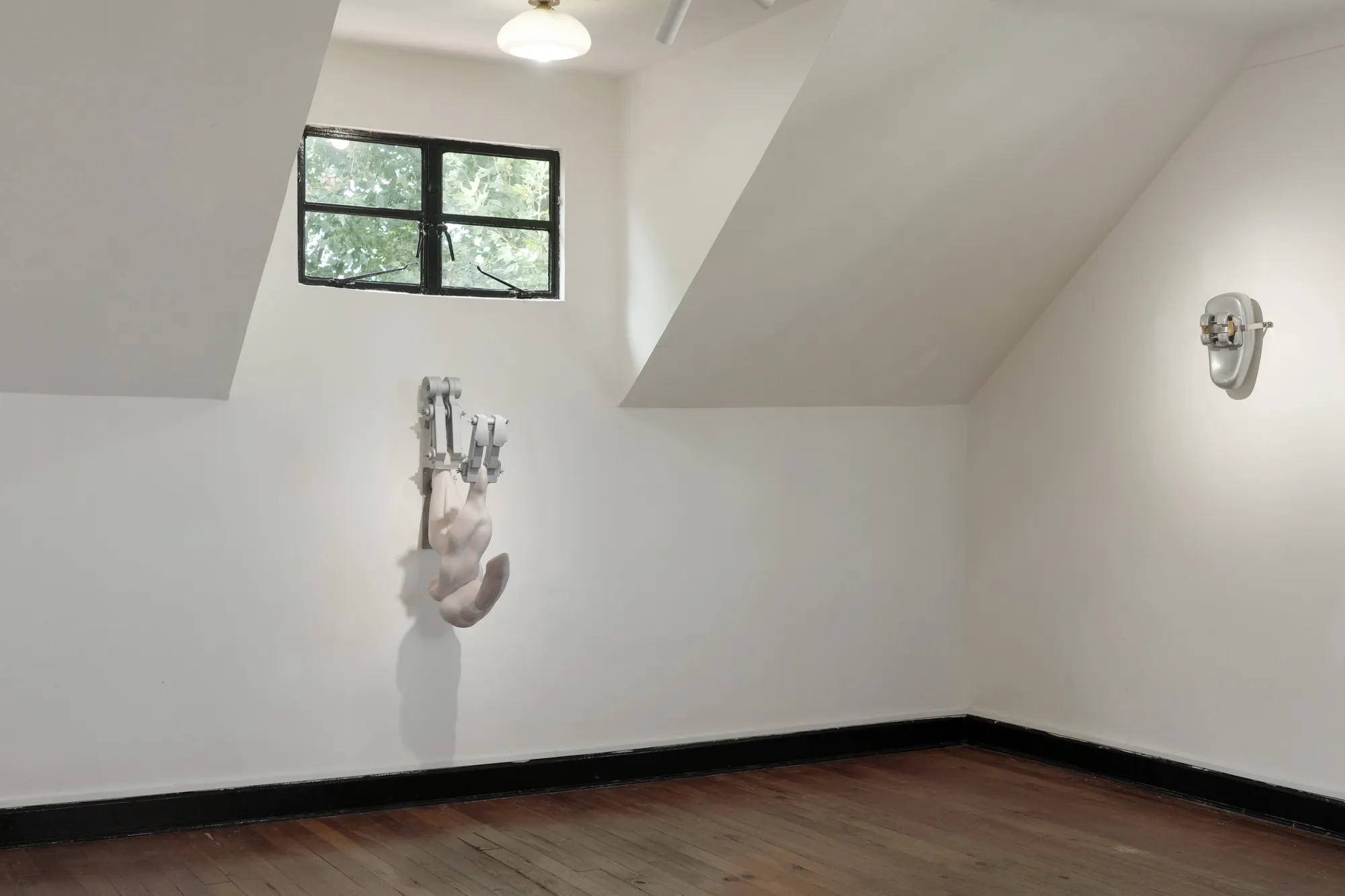Exhibition review of Eva Chenyao He: Procrustean at COLLECTA, Shanghai, 2026. A resin limb clamped in a steel bracket by a sloped ceiling.