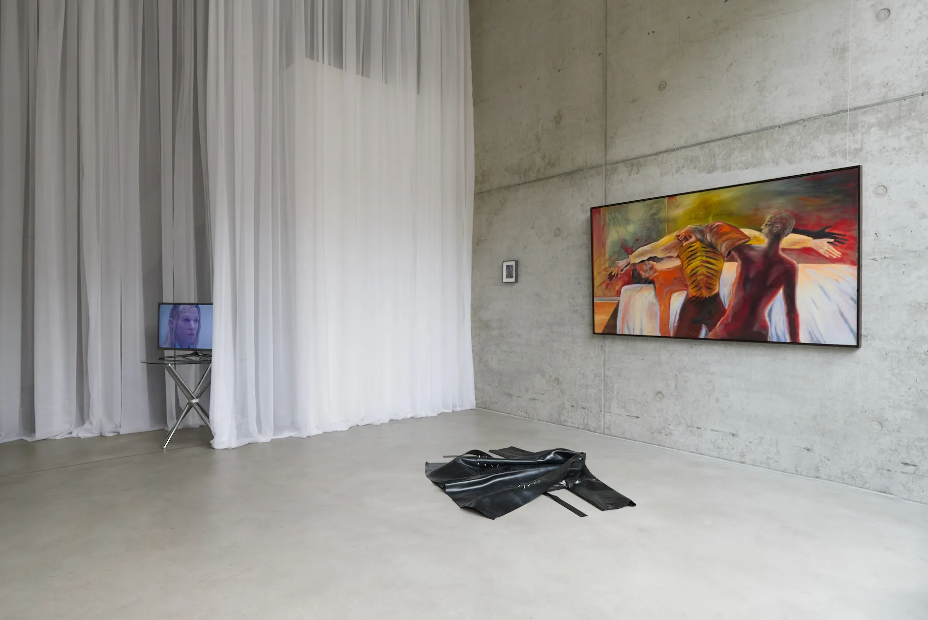 Exhibition review of I Think My Body No Longer Belongs to Me at roam projects e. V., Berlin, 2026. White curtains, monitor on glass table, painting, coat on floor.