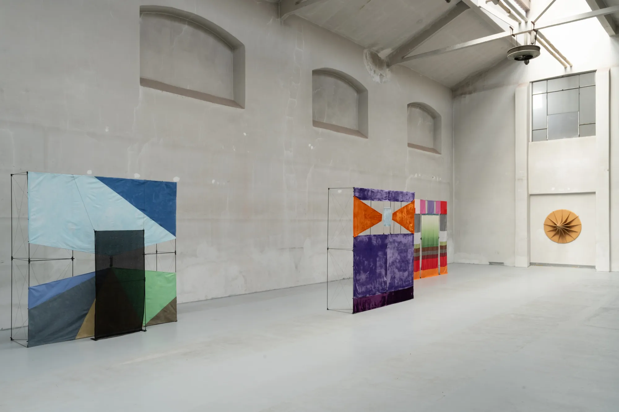 catapult contemporary Exhibition review of Tillmann Lauterbach and Weseeclearly: Field Work at Factory Eleven, Milan, 2026. Fabric screens angled across a large hall, with a folded tan fan-shaped relief on the far white wall.