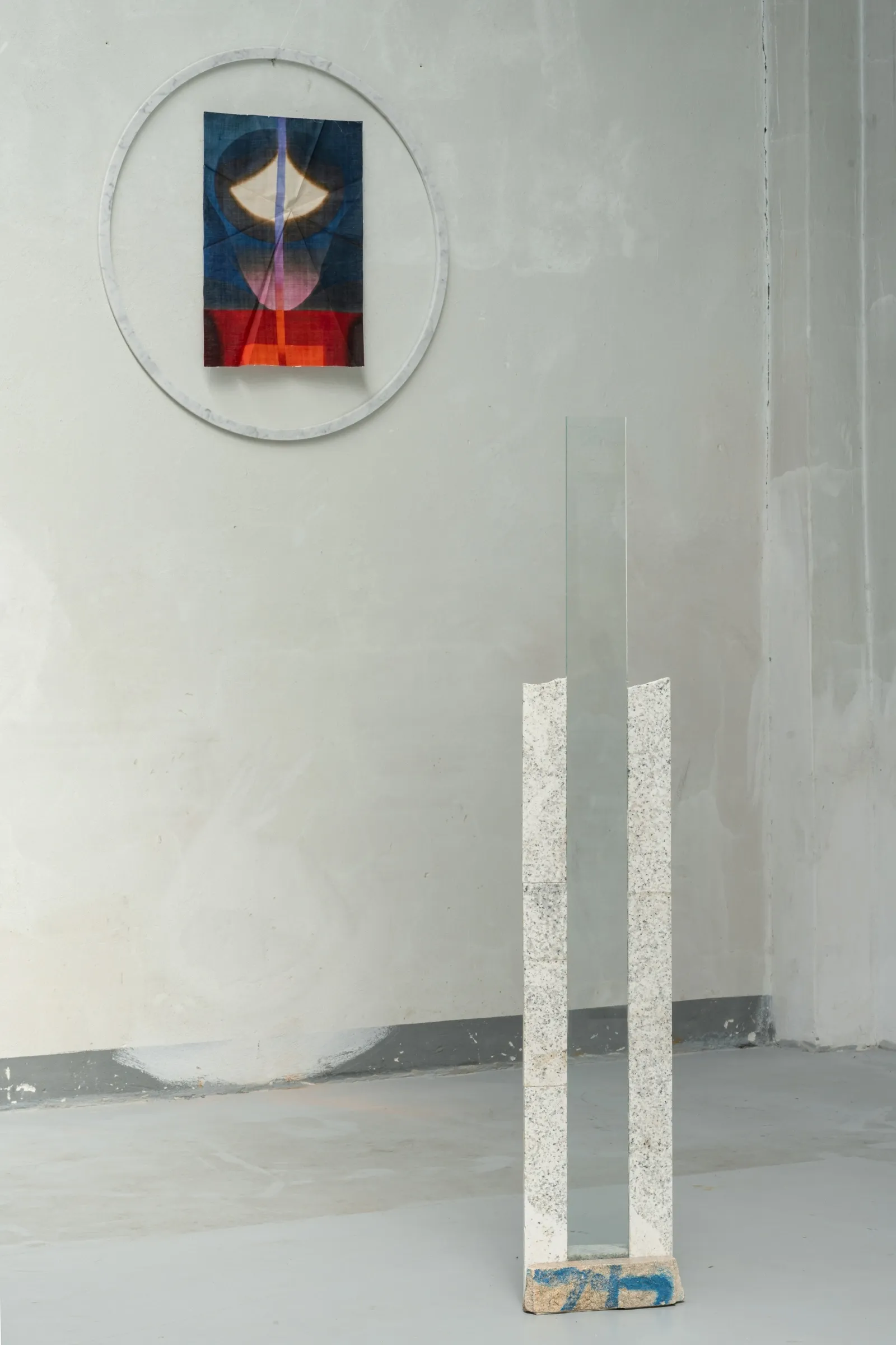 Exhibition review of Tillmann Lauterbach and Weseeclearly: Field Work at Factory Eleven, Milan, 2026. Tall glass pane set in a speckled stone base in front of a round frame holding a small textile.