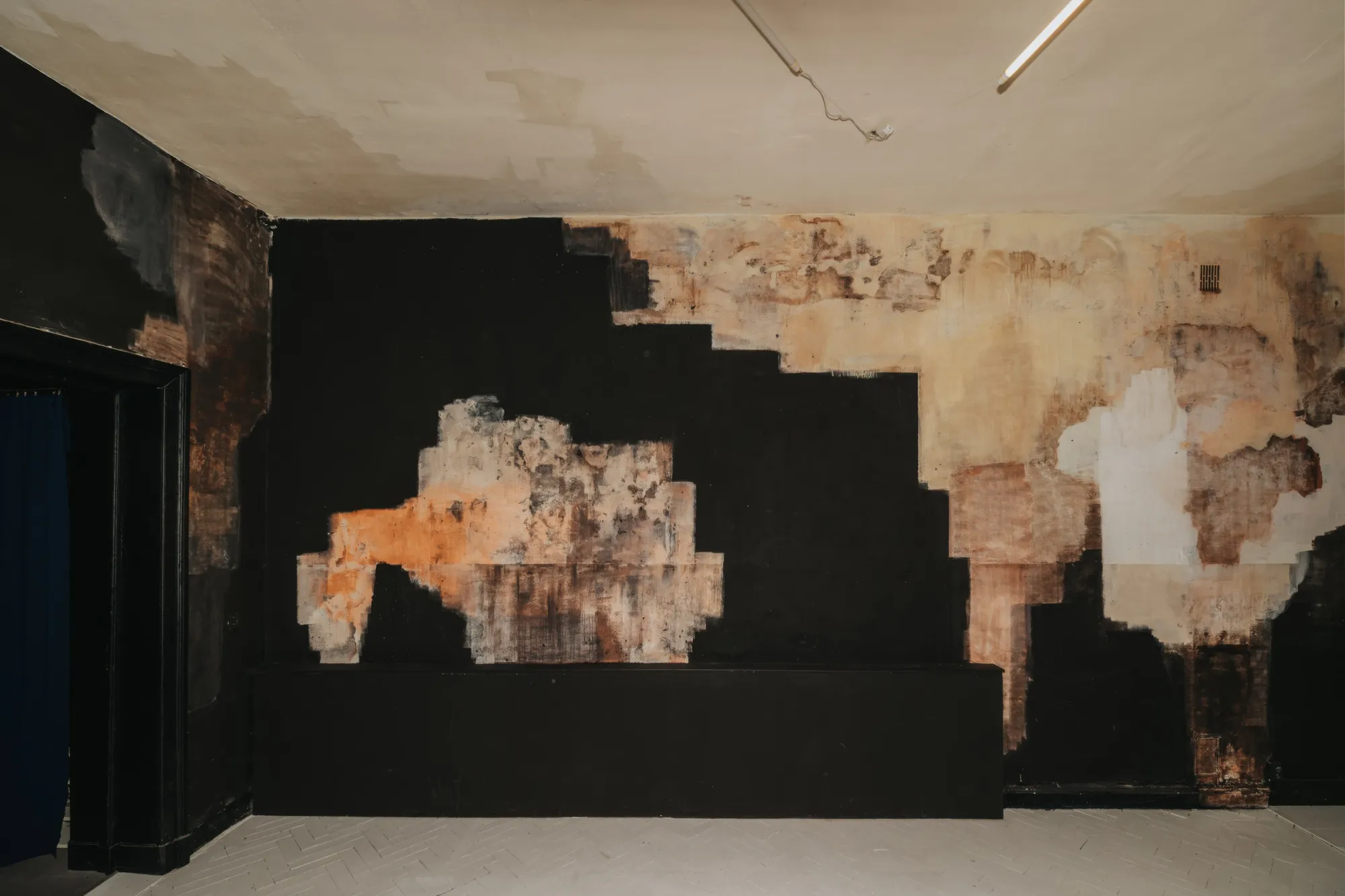 Exhibition review of Paulina Semkowicz: Residency: The Wall at Galeria S35, Łódź, 2026. Stepped black field with a free-floating patch of orange and grey pigment above a low black plinth.