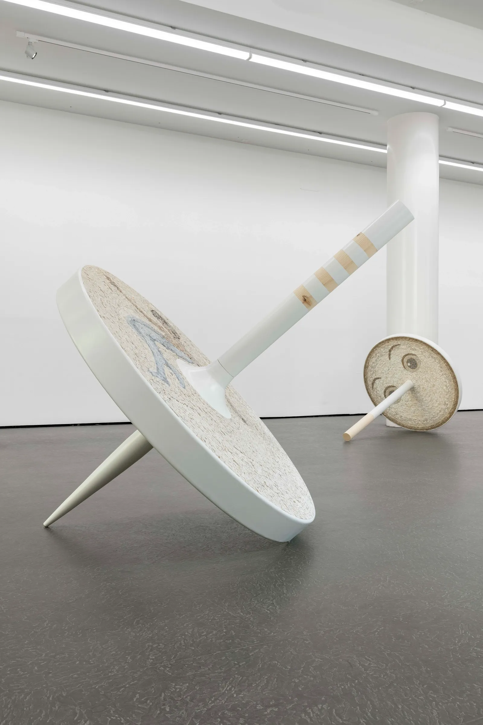 Exhibition review of Riikka Anttonen: Vertere at Sinne, Helsinki, 2026. Two large spinning-top sculptures crossed in an X shape on the gallery floor.