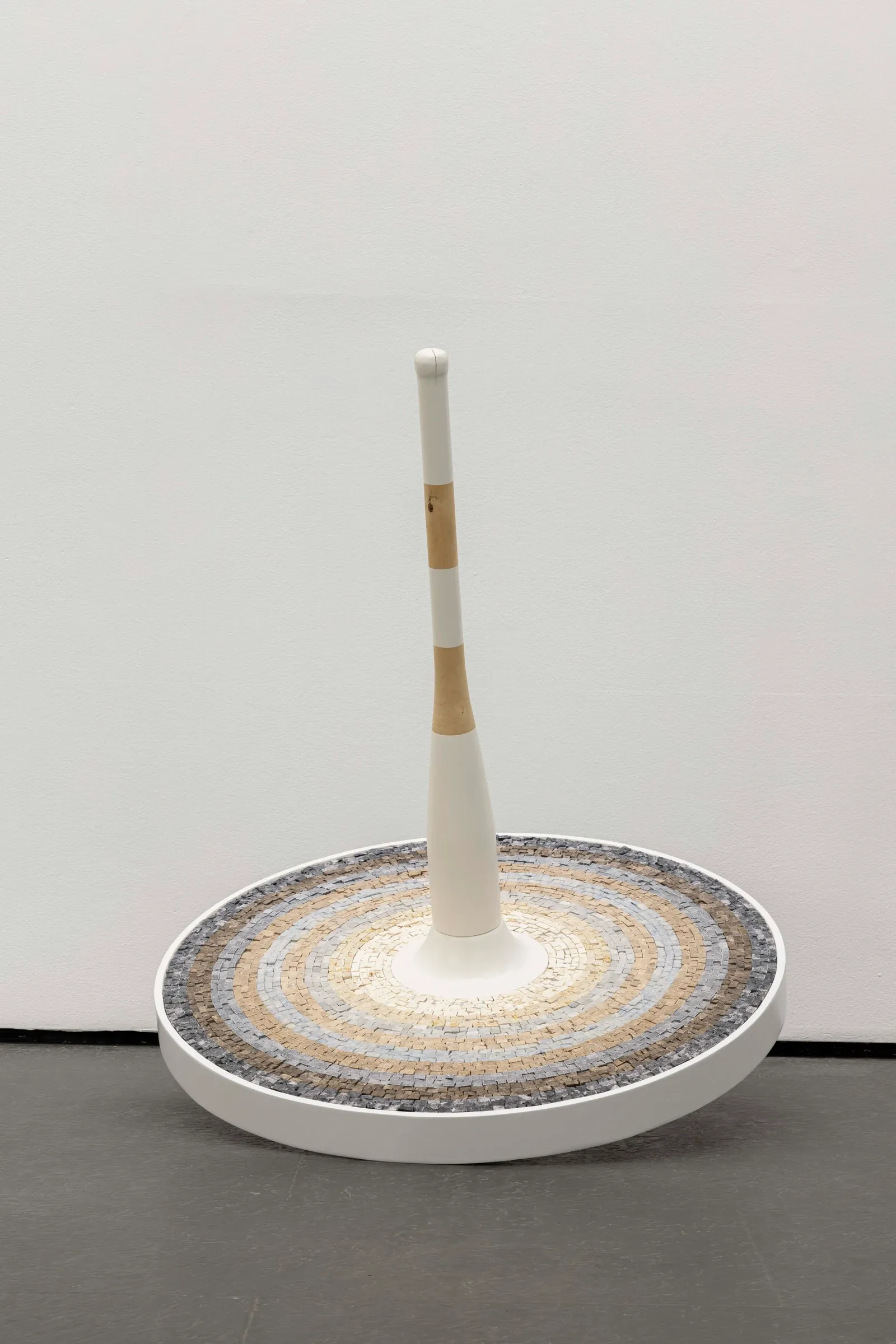 Exhibition review of Riikka Anttonen: Vertere at Sinne, Helsinki, 2026. White spinning-top sculpture with a raised clover-shaped relief pattern circling its disc.