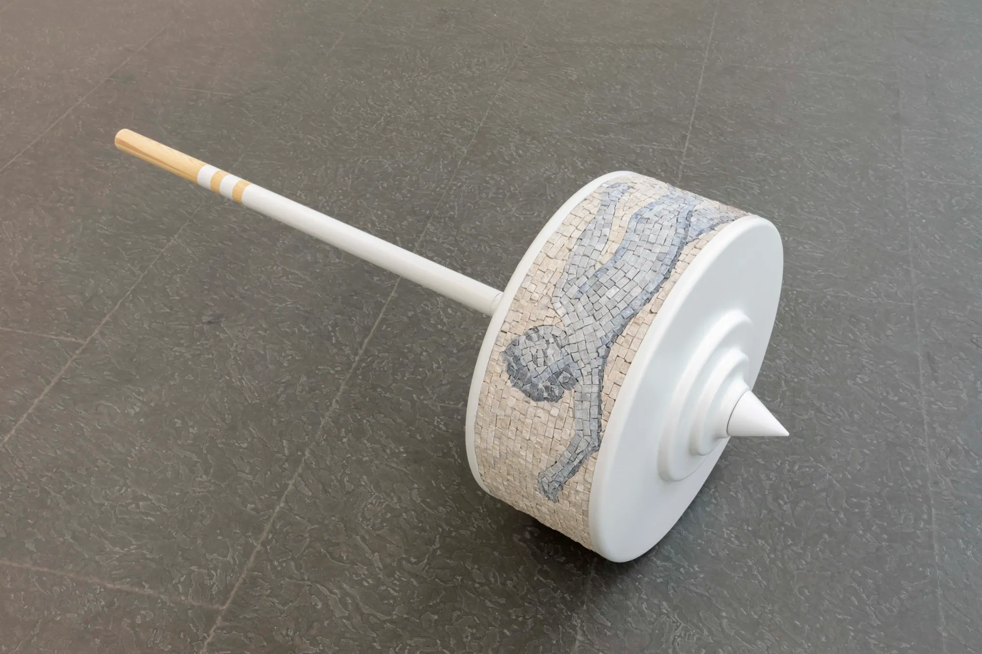 Exhibition review of Riikka Anttonen: Vertere at Sinne, Helsinki, 2026. Spinning-top sculpture with a leaping animal figure rendered in grey and cream marble mosaic along its rim.