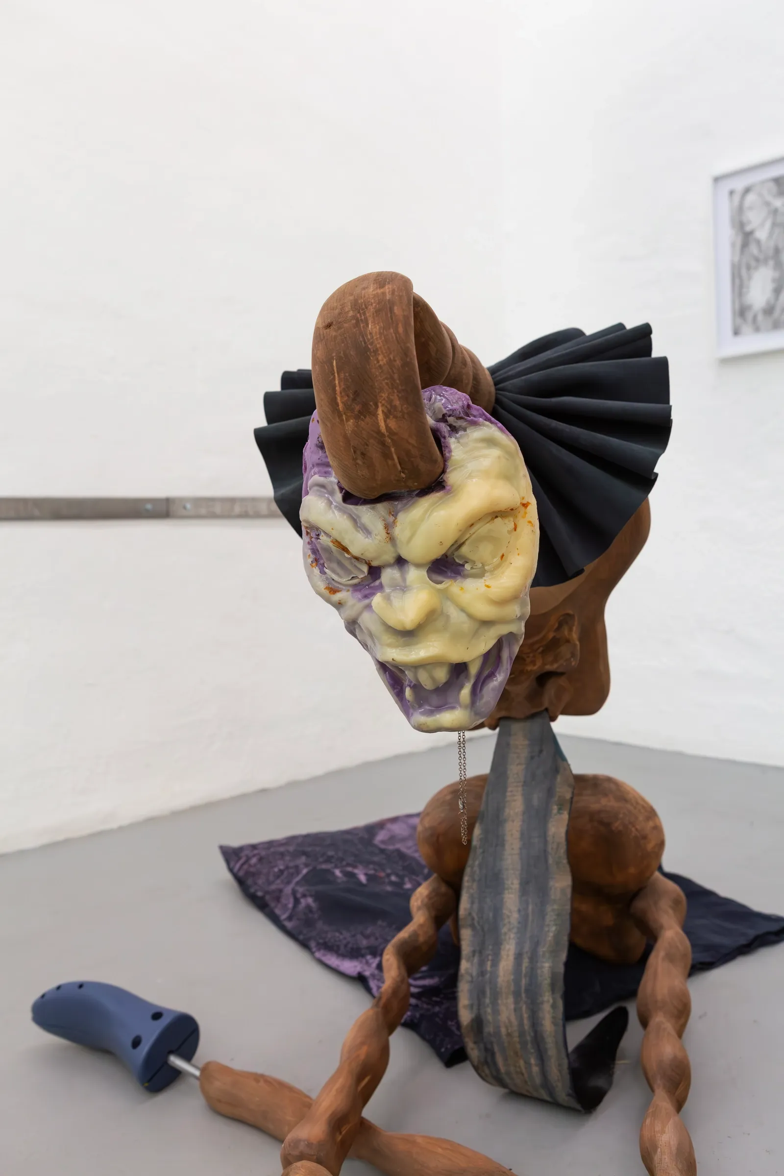 Exhibition review ofRaphaël Delannoy A Charm of Powerful Trouble at ACUD Galerie, Berlin, 2026. A seated papier-mâché figure with a grotesque painted mask, black fan-like collar, and lo