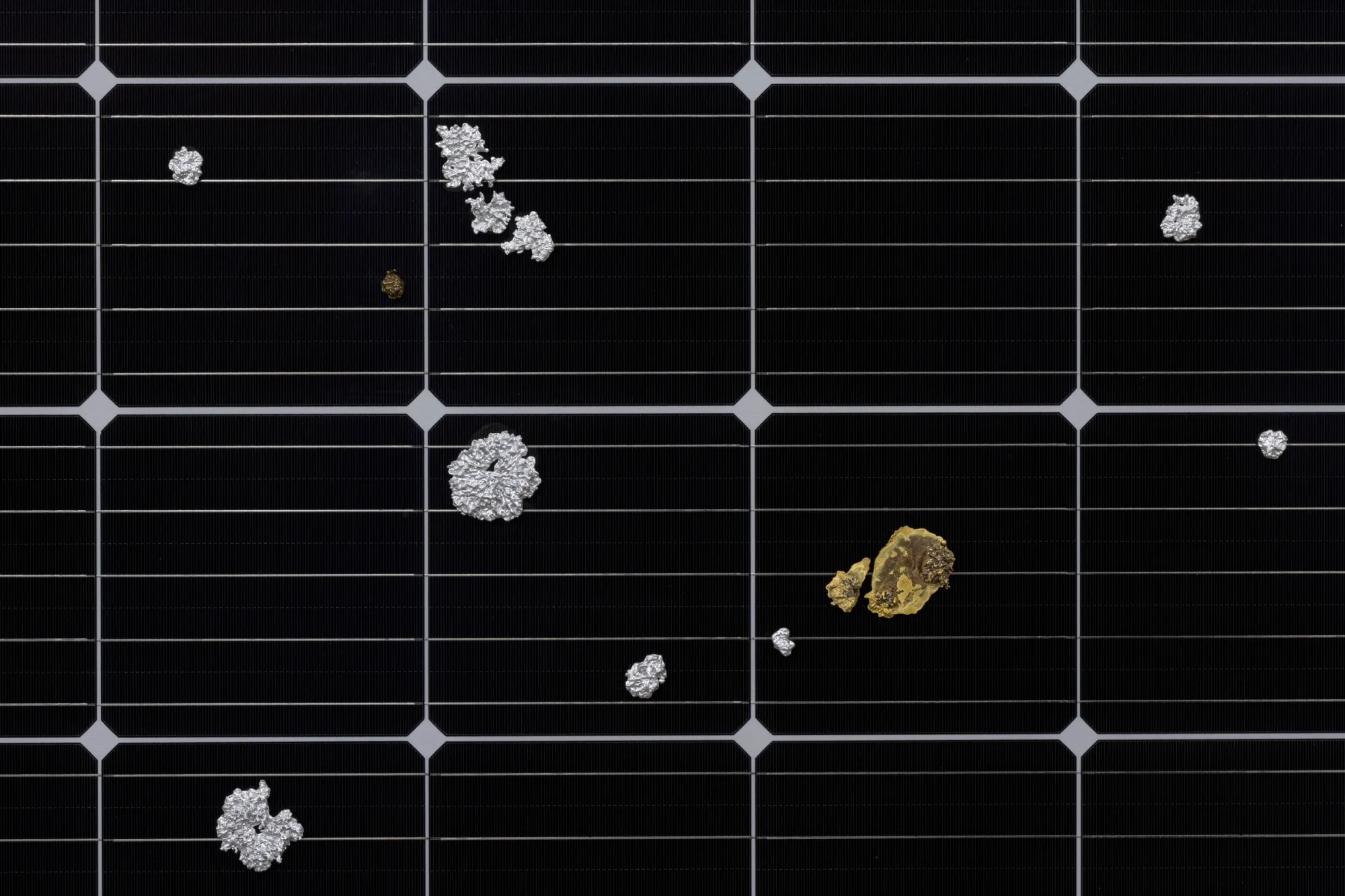 Exhibition review of Sari Palosaari: Substrate at Forum Box, Helsinki, 2026. Black solar panel surface with silver aluminium and gold brass lichen-shaped casts on its grid lines.