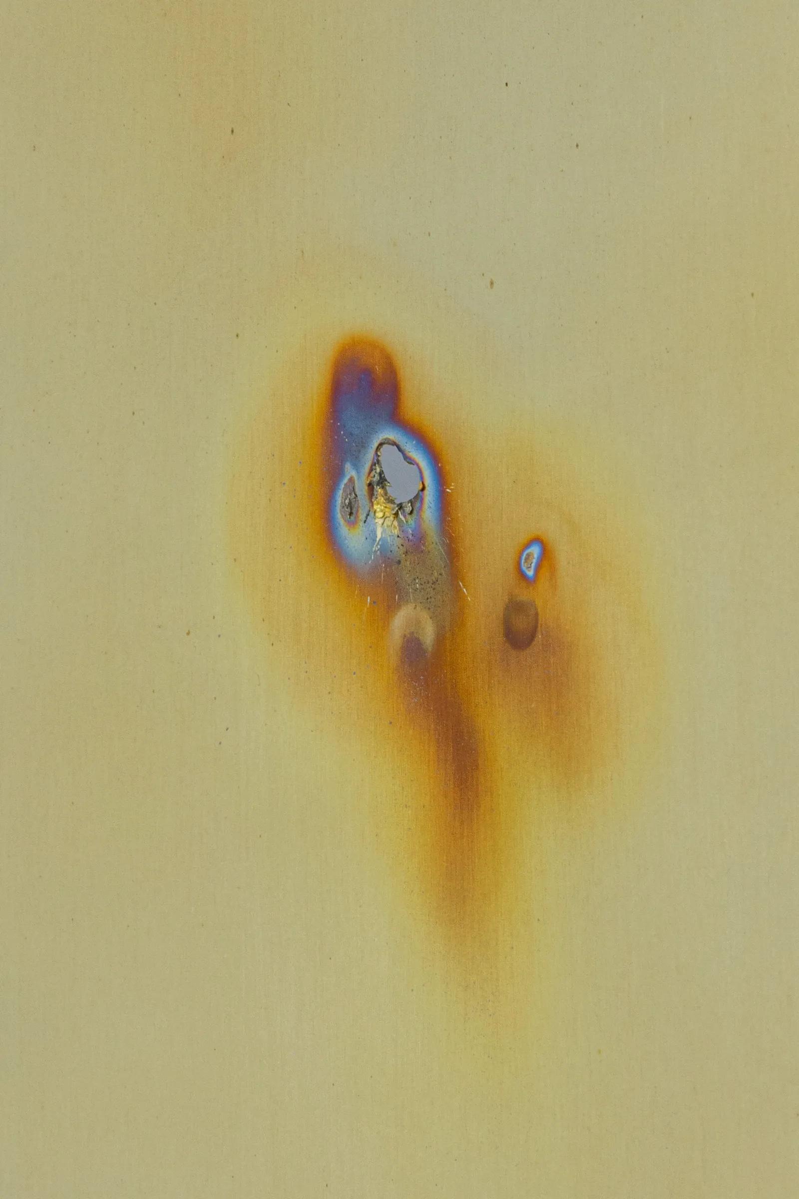 Exhibition review of Sari Palosaari: Substrate at Forum Box, Helsinki, 2026. Brass surface with a blue, violet and orange heat-tinted burn mark.