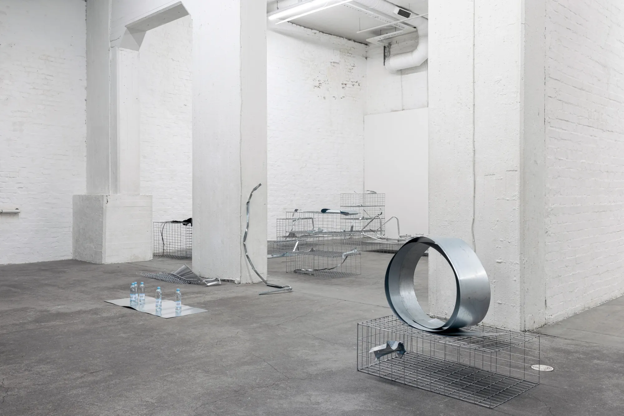 Exhibition review of Sari Palosaari: Substrate at Forum Box, Helsinki, 2026. Wire gabion baskets, a large galvanised metal ring and metal fragments spread across a concrete floor between white pillars.