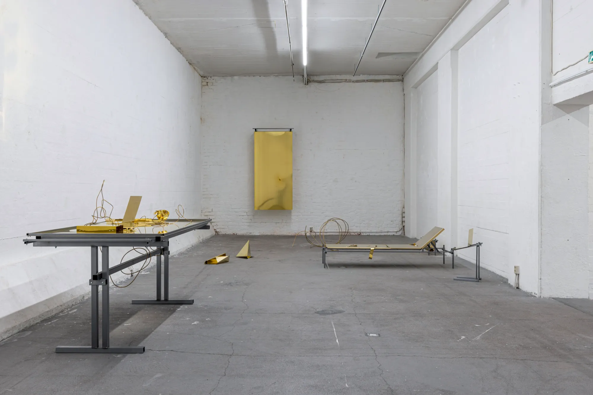 Exhibition review of Sari Palosaari: Substrate at Forum Box, Helsinki, 2026. Long white hall with a steel desk holding brass forms, a brass sheet on the back wall and a low brass-topped bench.