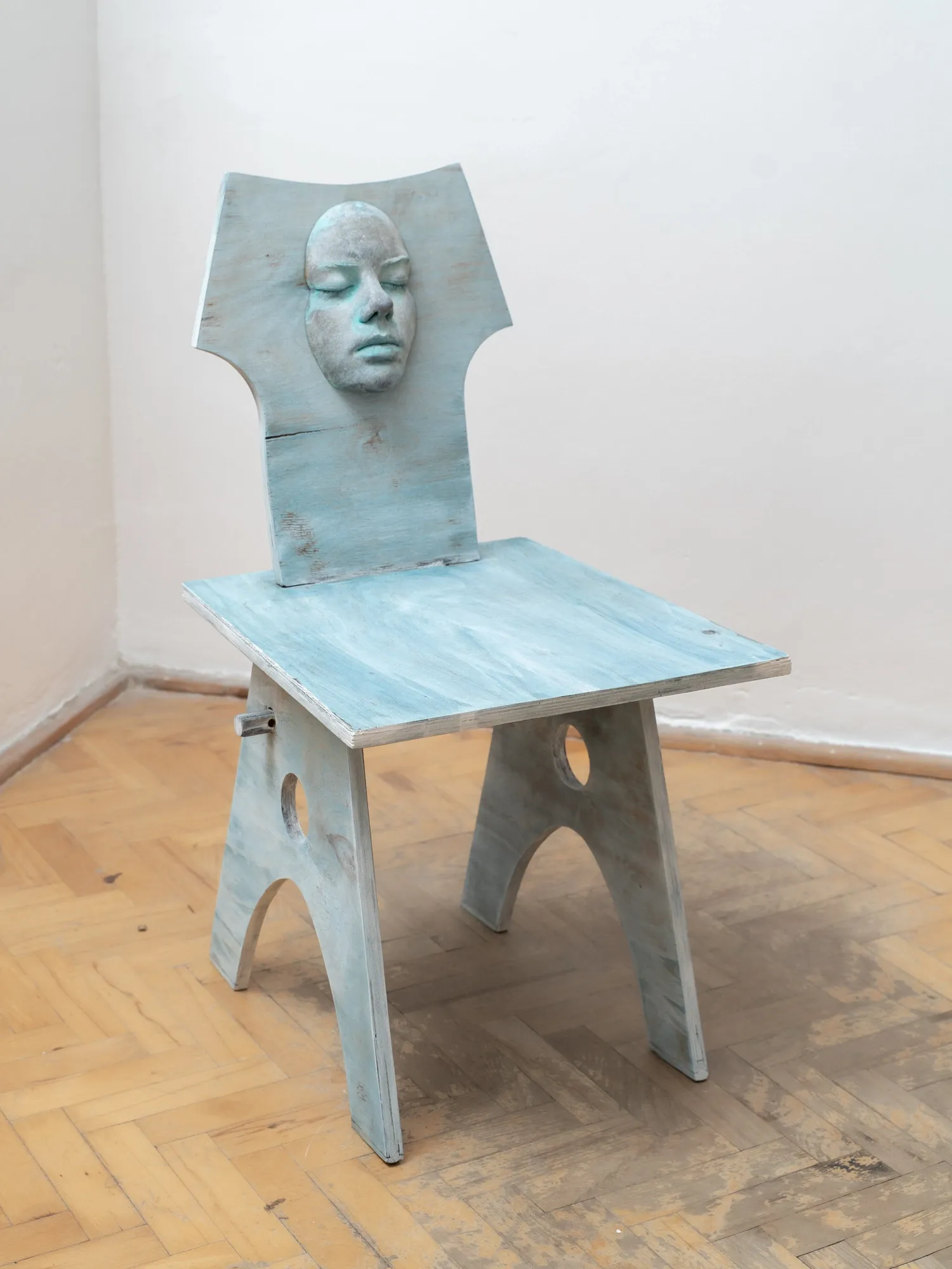Ała Wierzbicka, MISE EN, Warsaw: pale blue plywood chair with a cast face set into the backrest on a parquet floor.