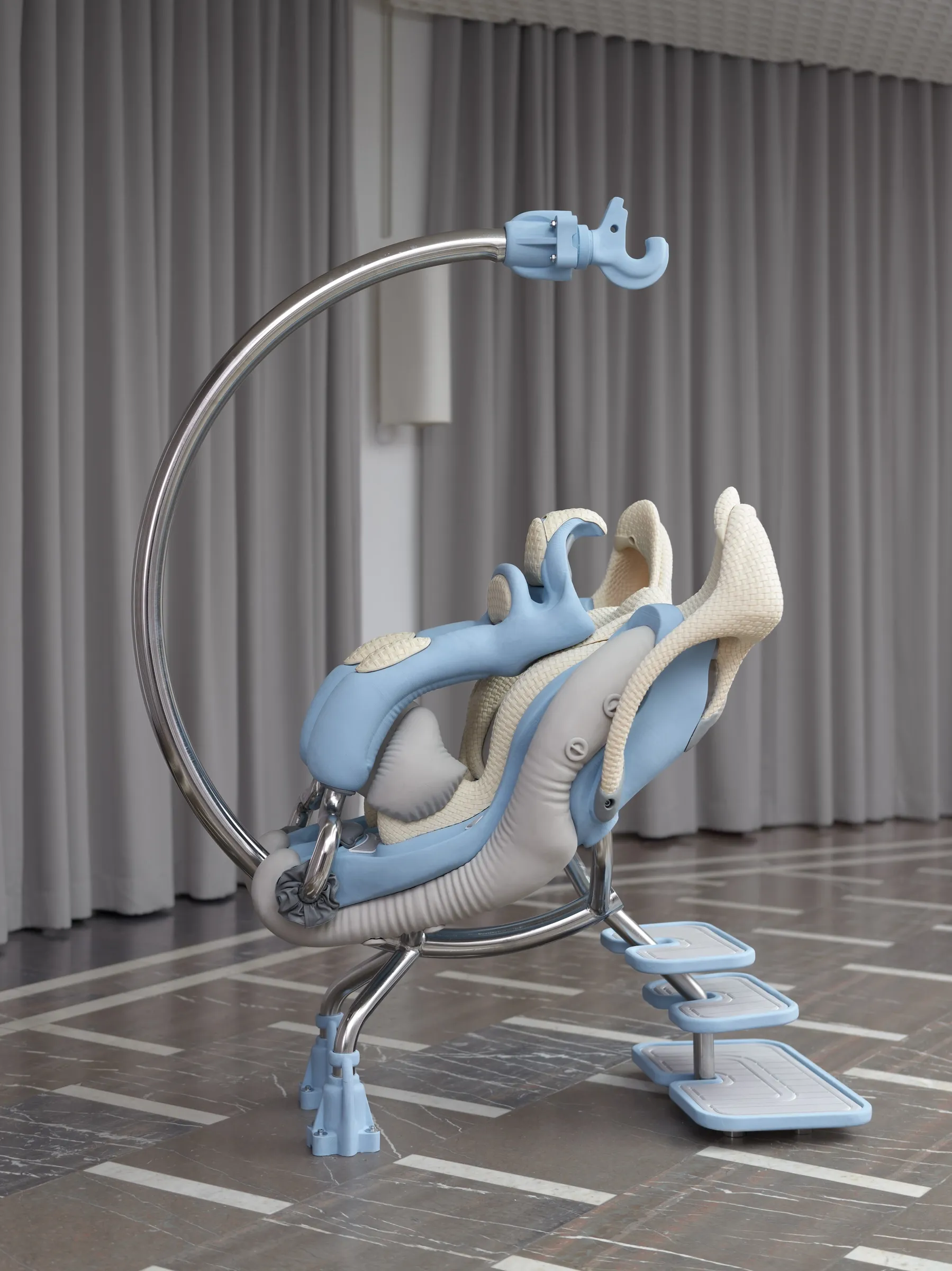 ALT: Anna Uddenberg, Telegraph Gallery, Olomouc: earlier sculpture Inflation, 2022, chrome arc with light blue shells and cream woven seats before grey curtains.