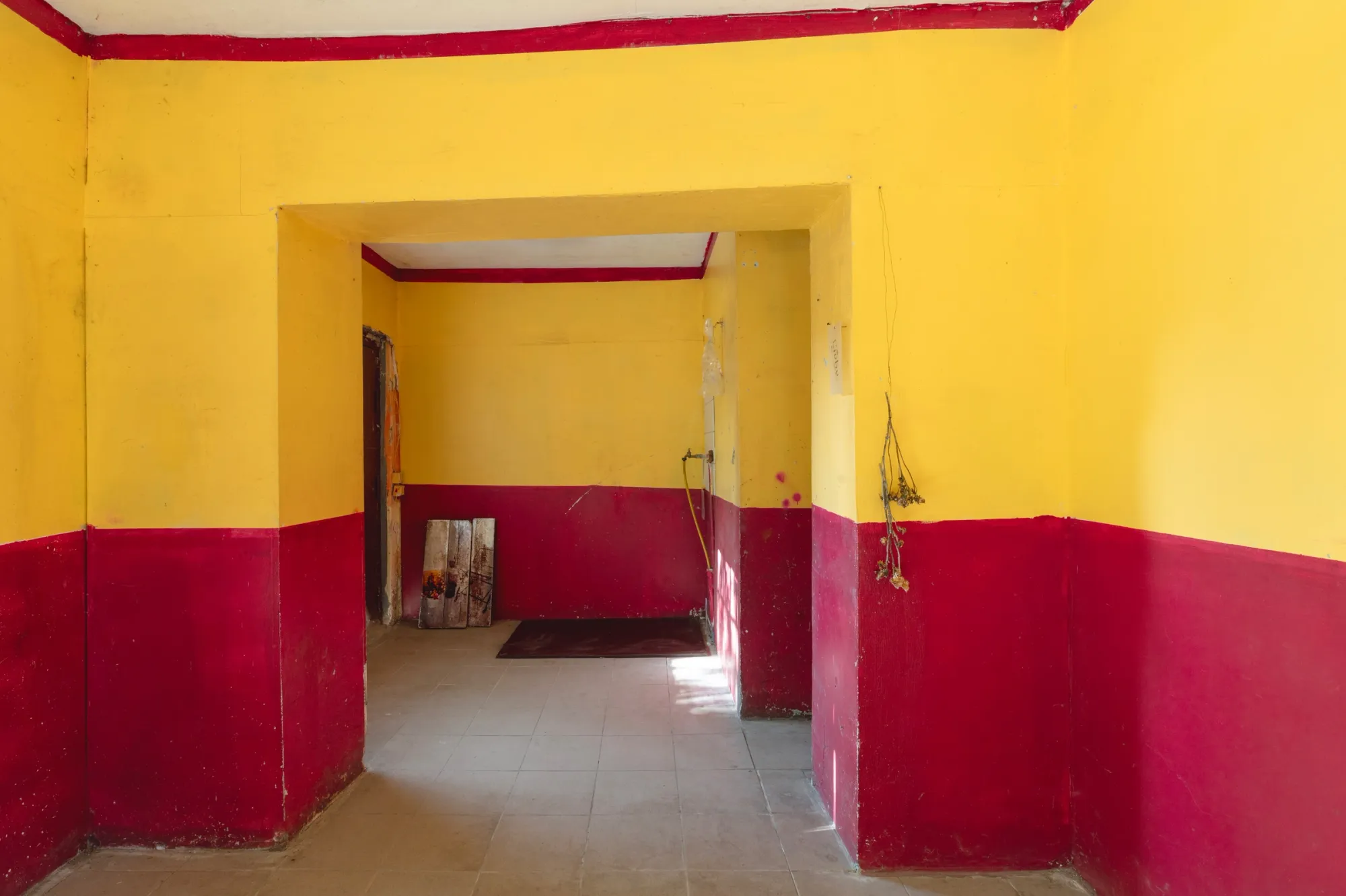 Aubrey&nbsp;Theobald&nbsp;and&nbsp;Kristina&nbsp;Popov,&nbsp;Phantom&nbsp;Pförtnerhaus&nbsp;Chapter&nbsp;3,&nbsp;Berlin,&nbsp;2026.&nbsp;Doorway&nbsp;between&nbsp;yellow&nbsp;and&nbsp;crimson&nbsp;exhibition&nbsp;rooms&nbsp;with&nbsp;a&nbsp;dried&nbsp;plant&nbsp;hanging&nbsp;beside&nbsp;it.