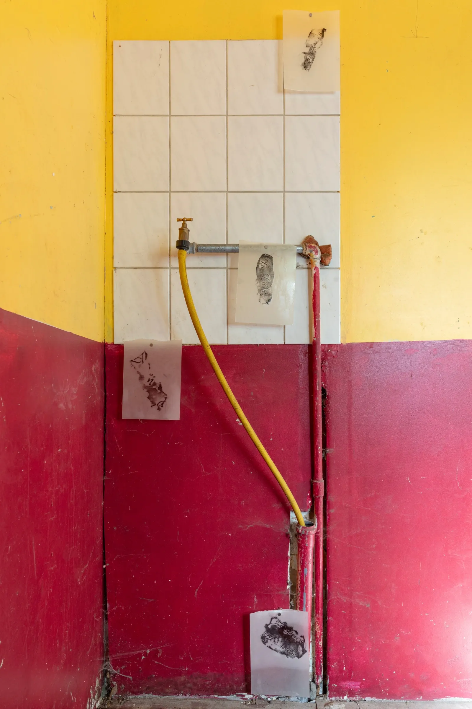 Aubrey&nbsp;Theobald&nbsp;and&nbsp;Kristina&nbsp;Popov,&nbsp;Phantom&nbsp;Pförtnerhaus&nbsp;Chapter&nbsp;3,&nbsp;Berlin,&nbsp;2026.&nbsp;White&nbsp;tiled&nbsp;wall&nbsp;with&nbsp;a&nbsp;tap,&nbsp;yellow&nbsp;hose&nbsp;and&nbsp;small&nbsp;translucent&nbsp;sheets&nbsp;bearing&nbsp;dark&nbsp;ink&nbsp;impressions.
