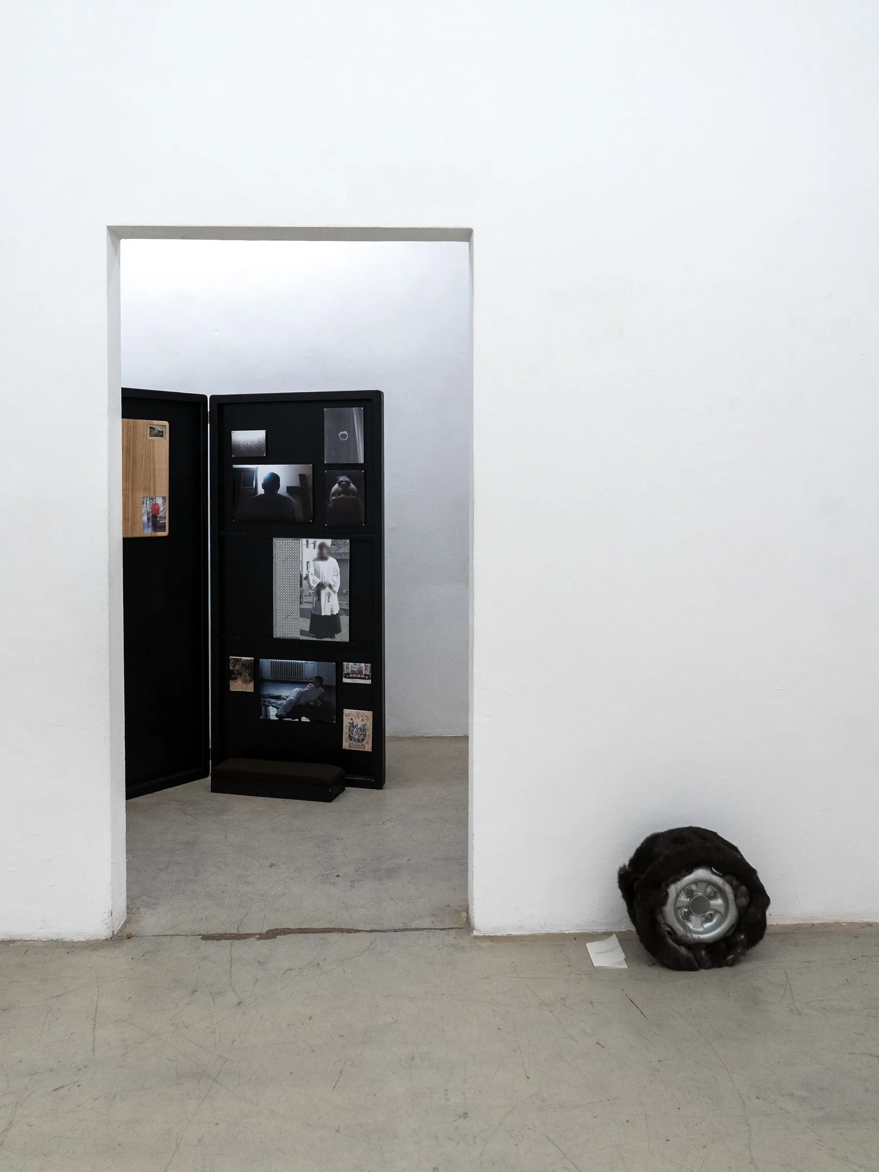 Exhibition review of AUSGEWEIDET / GUTTED at WAF Galerie, Vienna, 2026. Doorway view of a black hinged screen with photographs and a fur-wrapped rim.