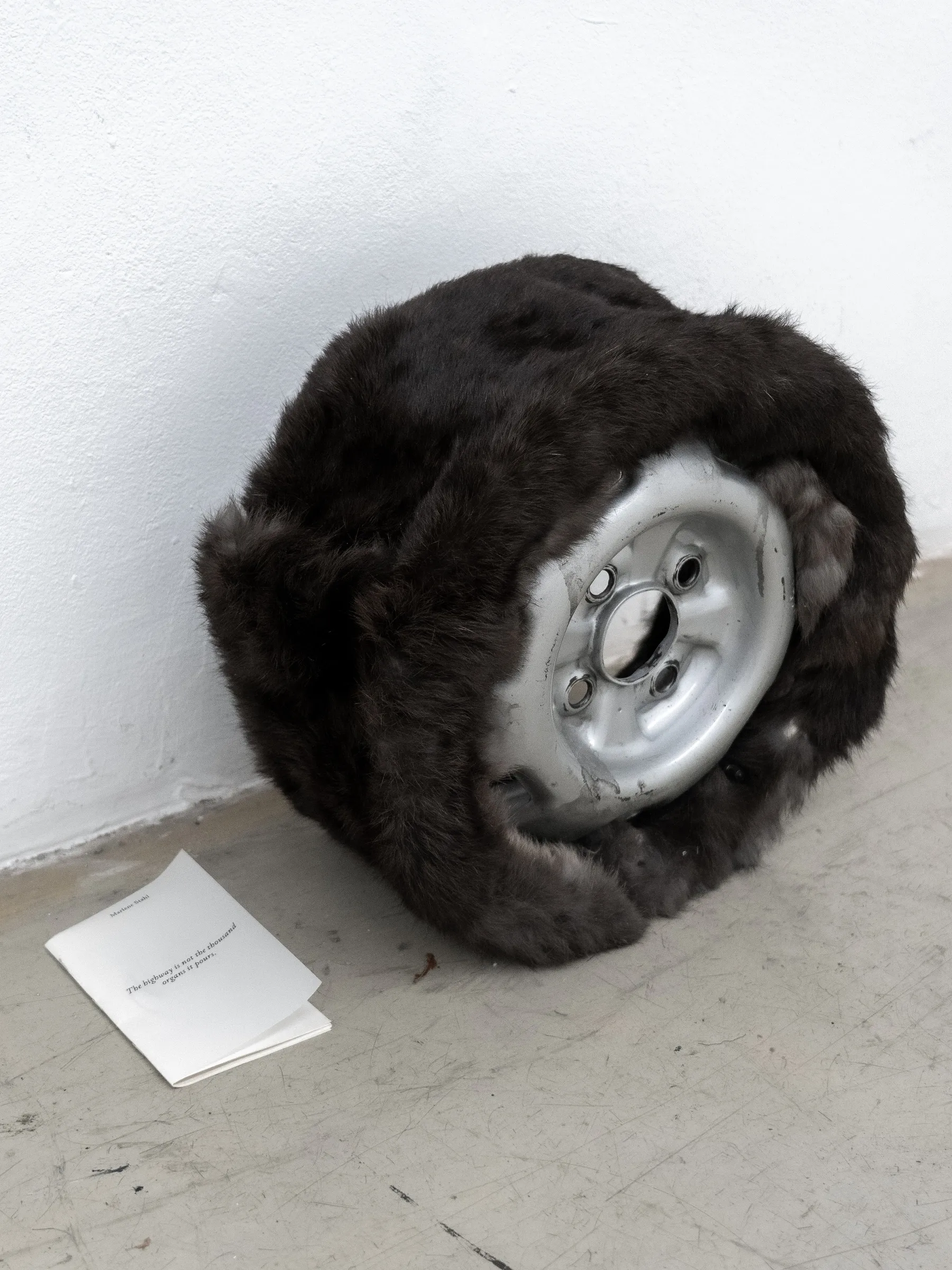 waf gallery vienna, current exhibition curated by leonie holtkamp, vienna ilver car rim wrapped in dark fur, a folded leaflet on the floor.
