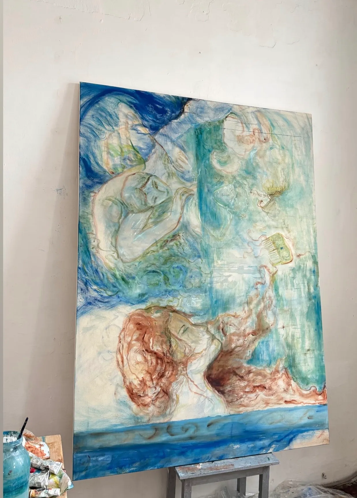 ALT: Christina Arark: large blue and green painting with figures, leaning on an easel in the studio.