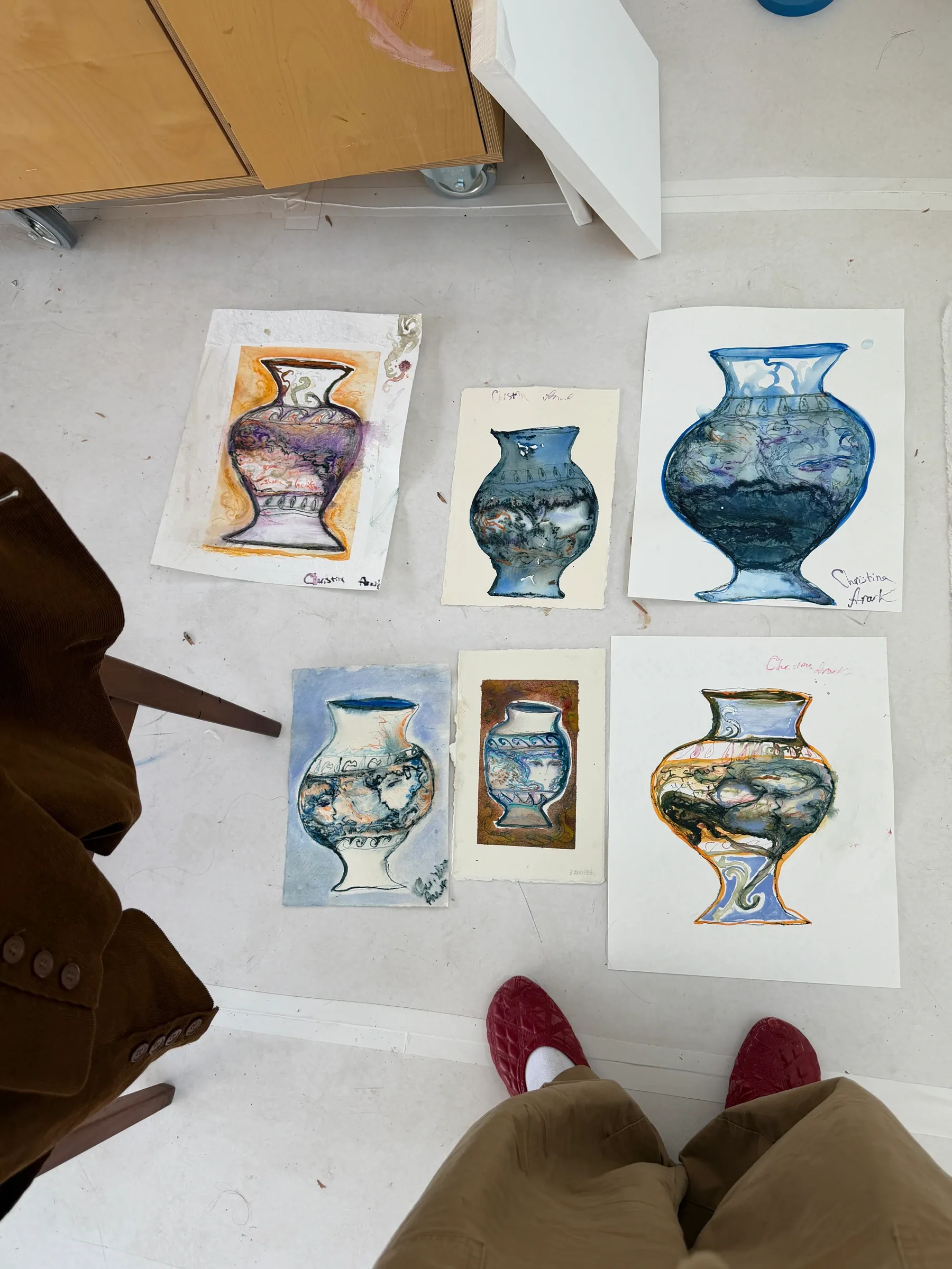 Six colourful drawings of decorated ceramic vases by Christina Arark, arranged on the floor with intricate patterns and figurative details.